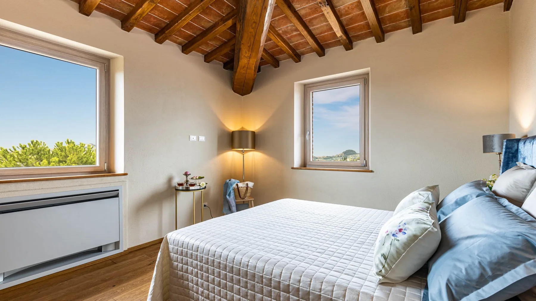 A bedroom with a bed beneath a sloped wooden-beam ceiling and two windows.