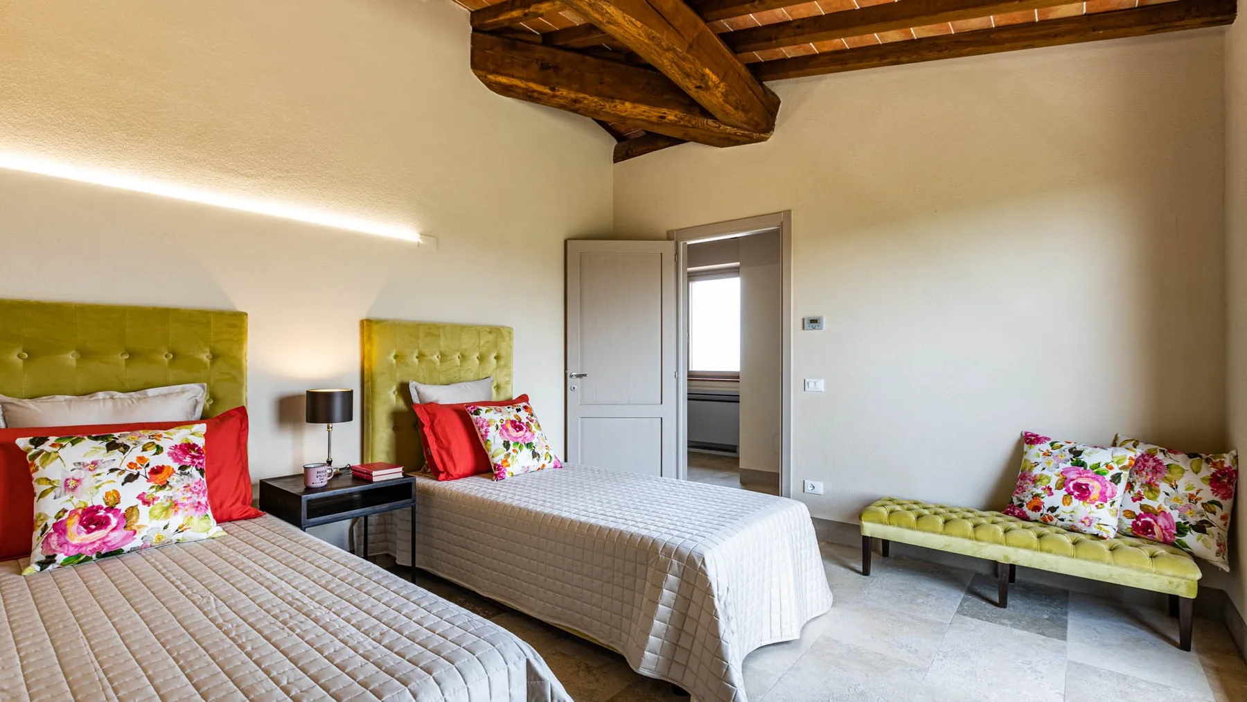 Bedroom with two beds and a small bench beneath exposed wooden ceiling beams.
