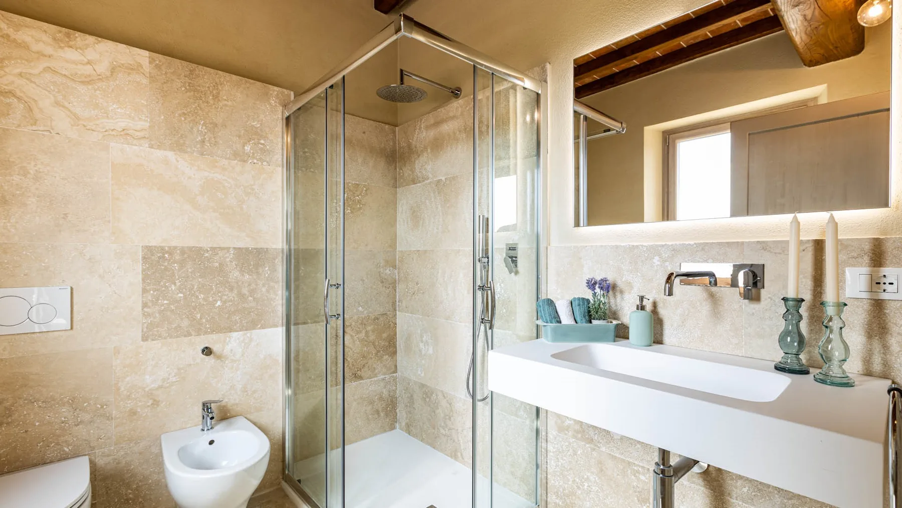 A bright bathroom with a glass shower and a long white sink.