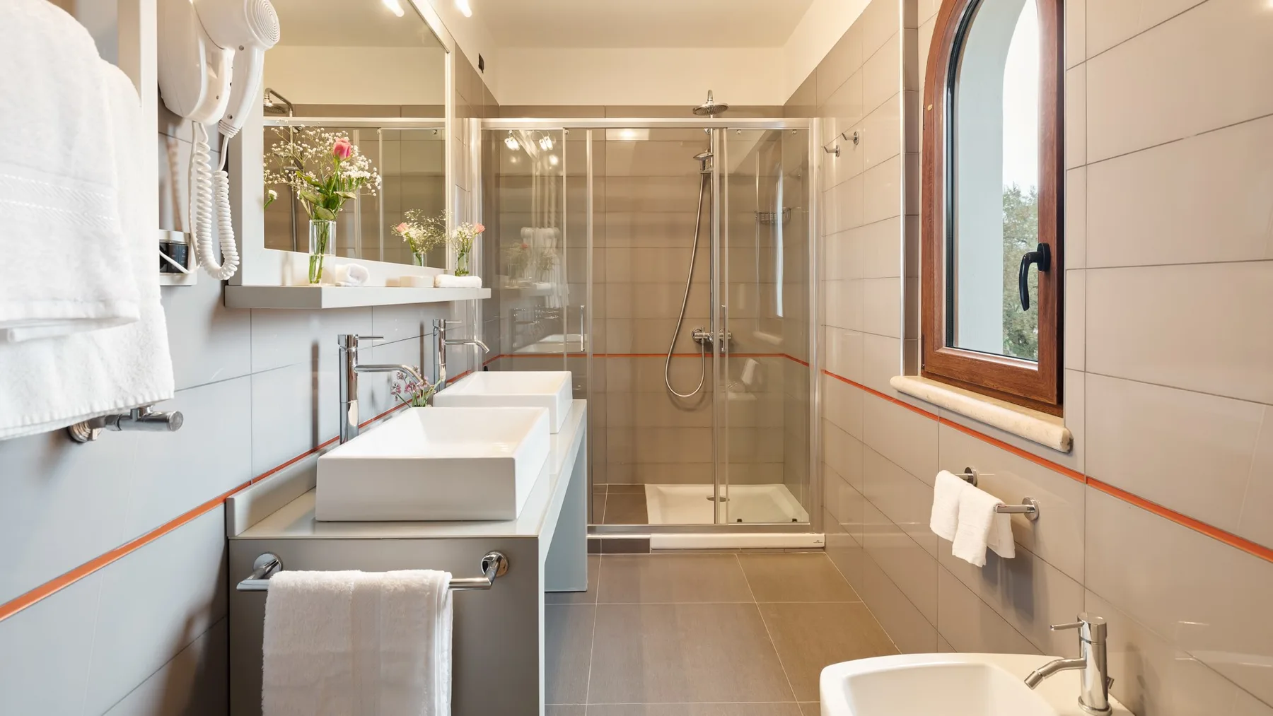 A bright bathroom with a glass shower and a long vanity.