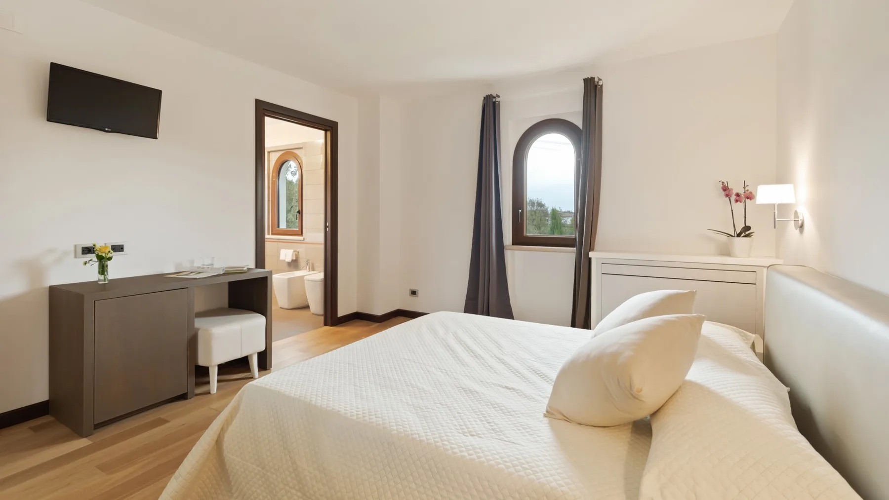 A bright bedroom with a neatly made bed and a desk beside the doorway.