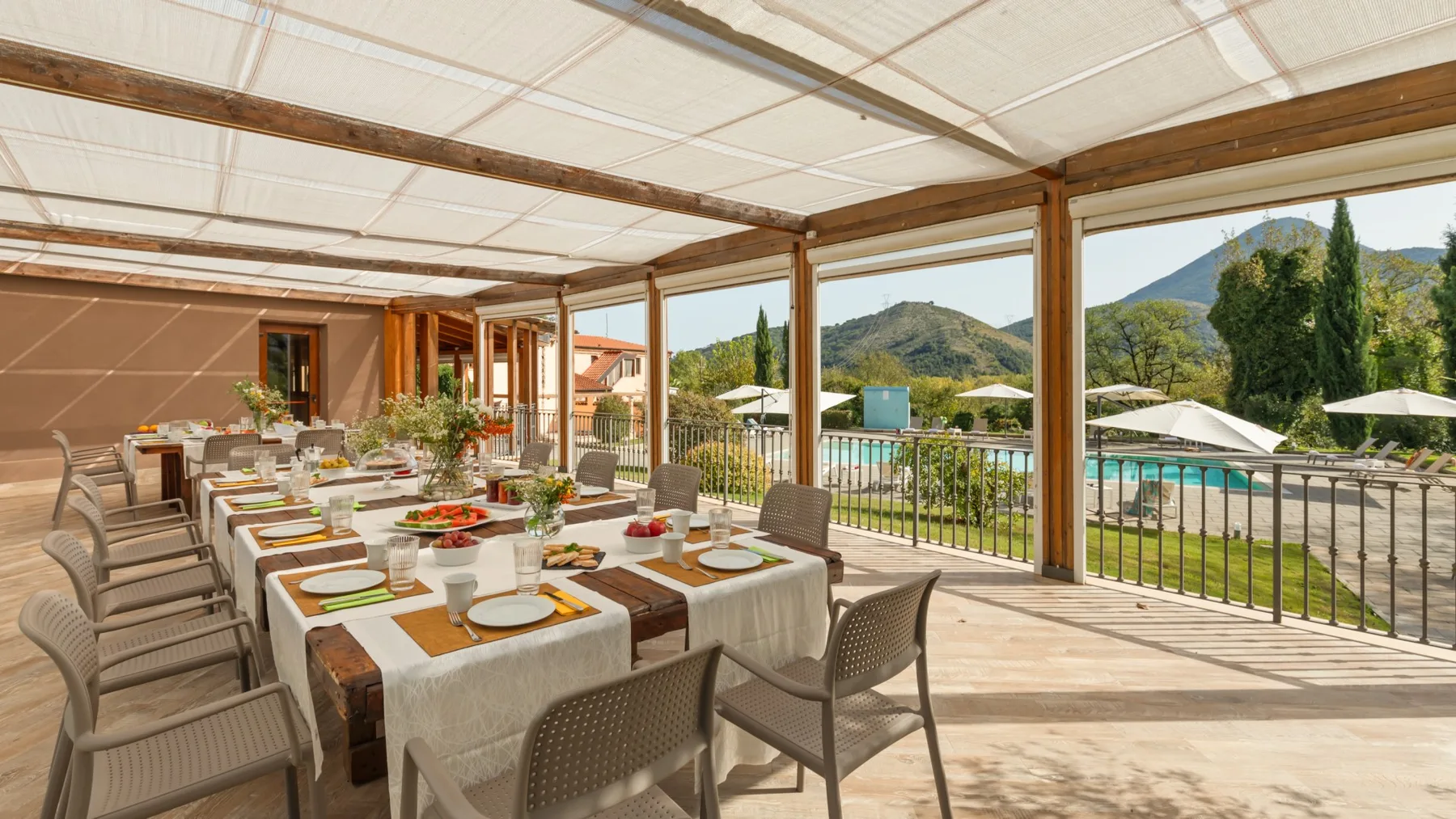 A covered outdoor dining area overlooks a swimming pool and green hills.