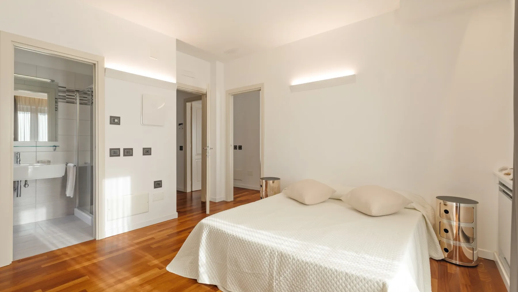 A bright bedroom with a neatly made bed and an adjoining bathroom.
