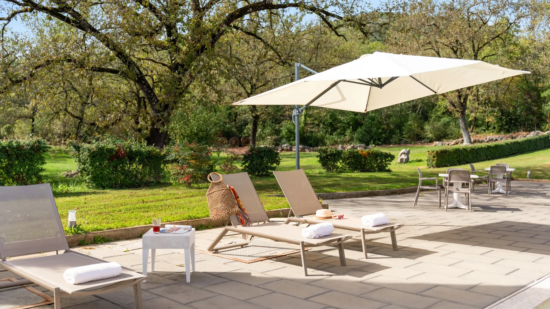 A patio with lounge seating and a large sun umbrella overlooks a green garden.