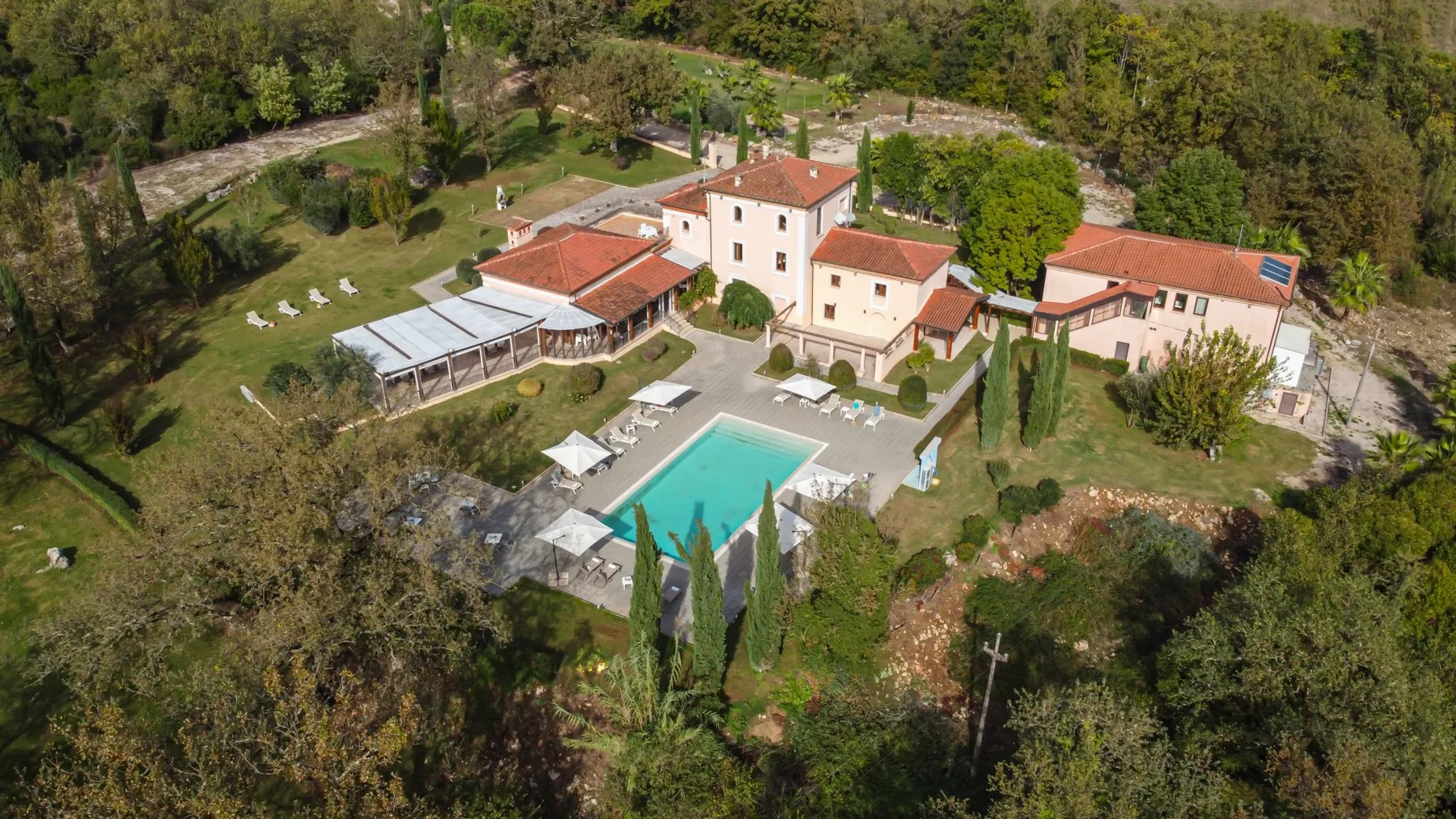 Aerial view of a countryside property with a swimming pool and surrounding trees.