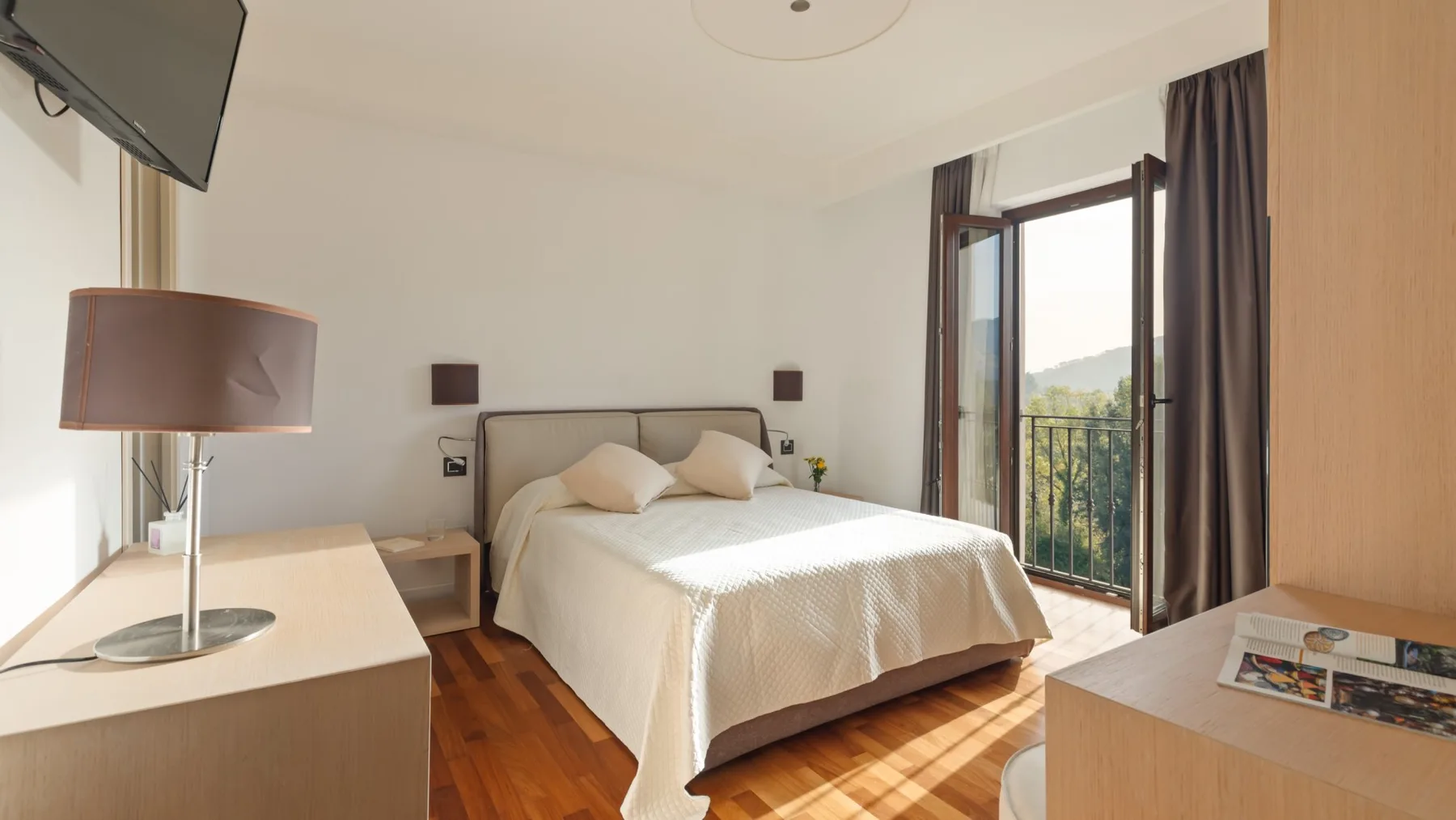 A bedroom with a neatly made bed and an open balcony door.