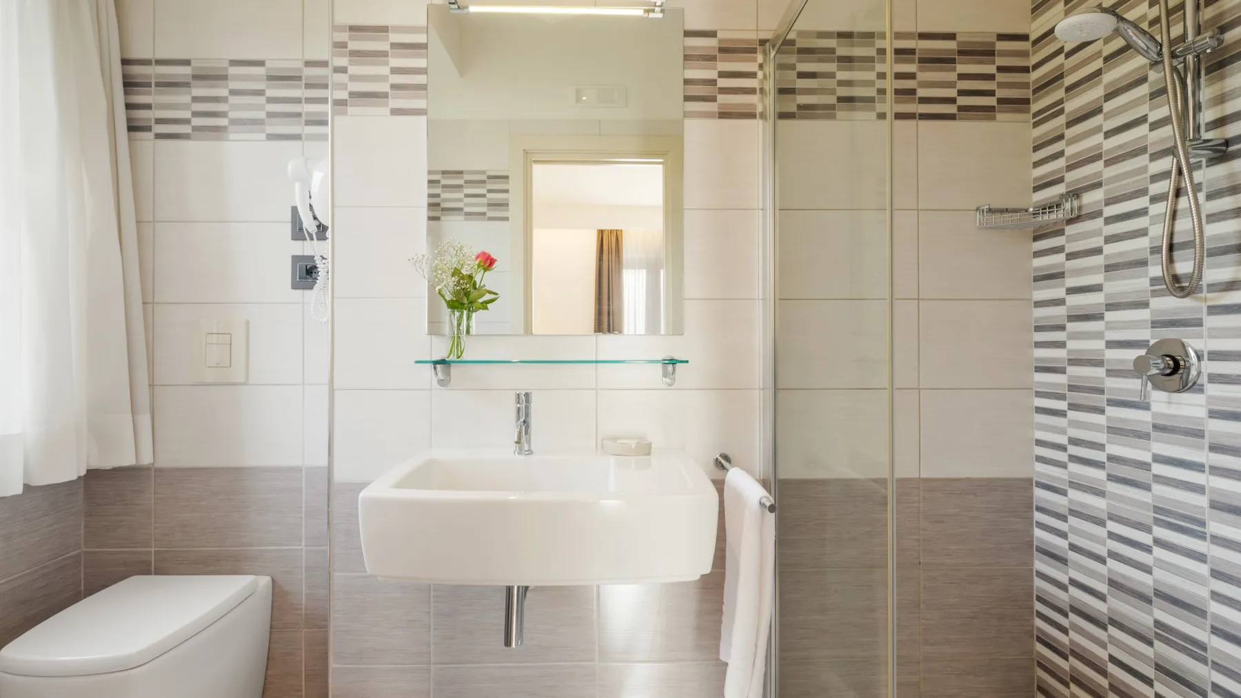 A tiled bathroom with a sink, mirror, toilet, and shower.
