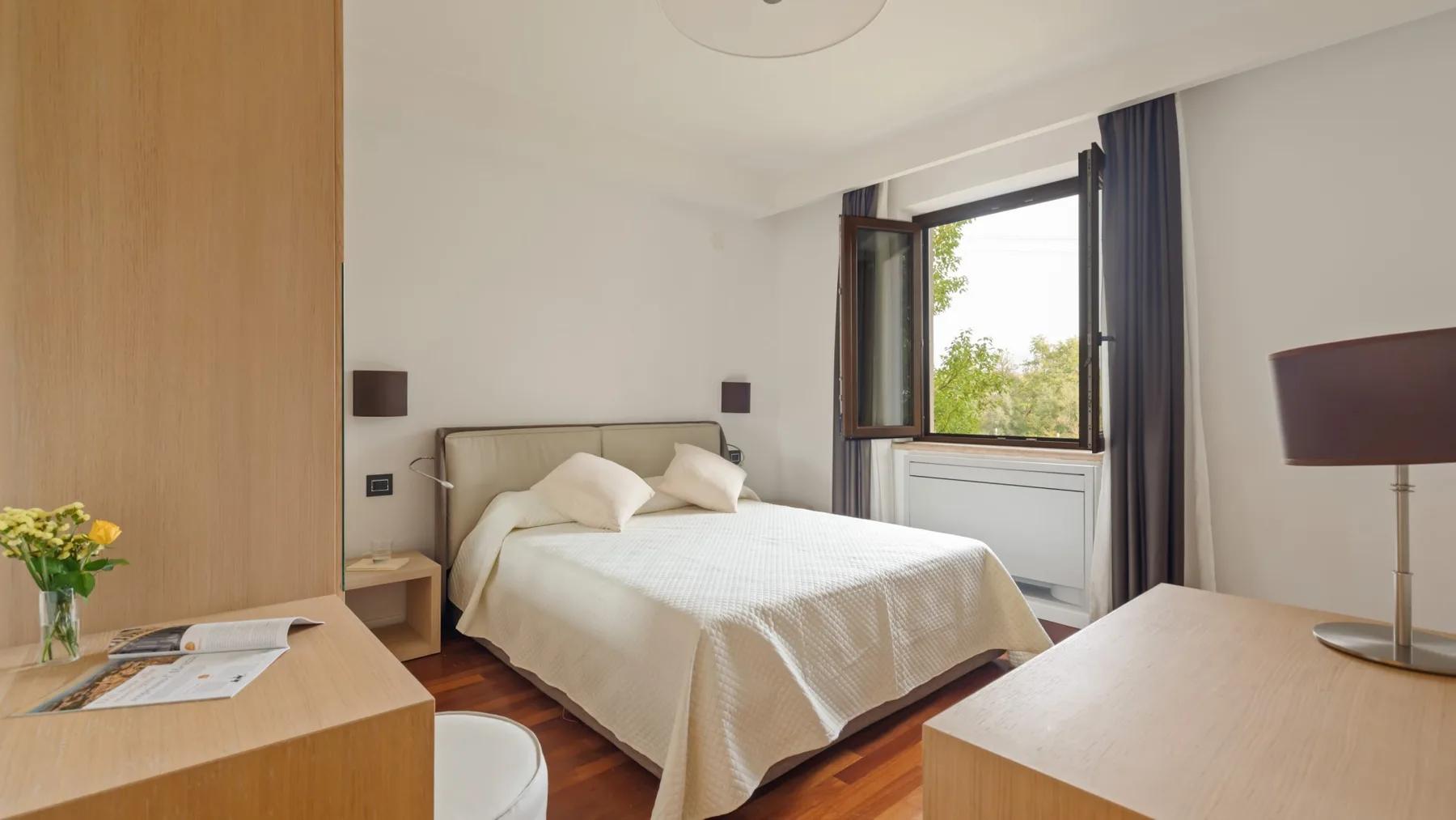 A bright bedroom with a neatly made bed and an open window.
