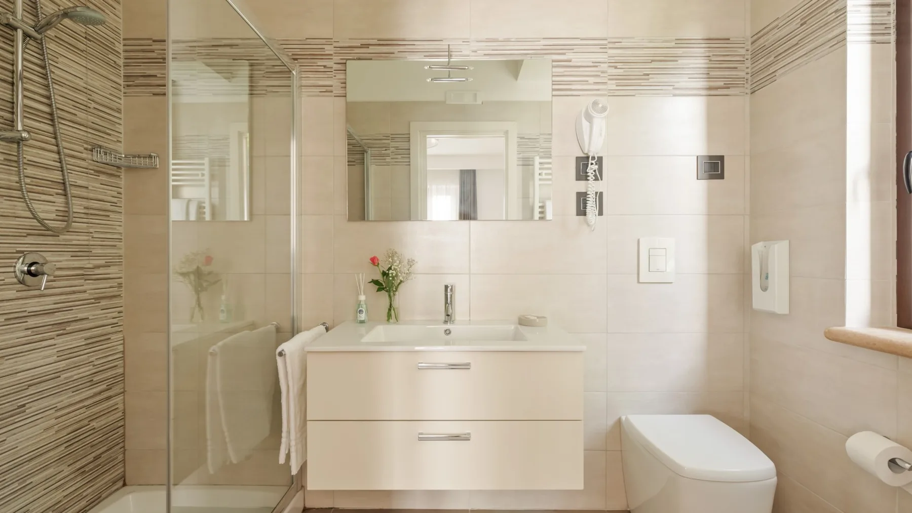 A bright bathroom with a glass shower, vanity, and toilet.