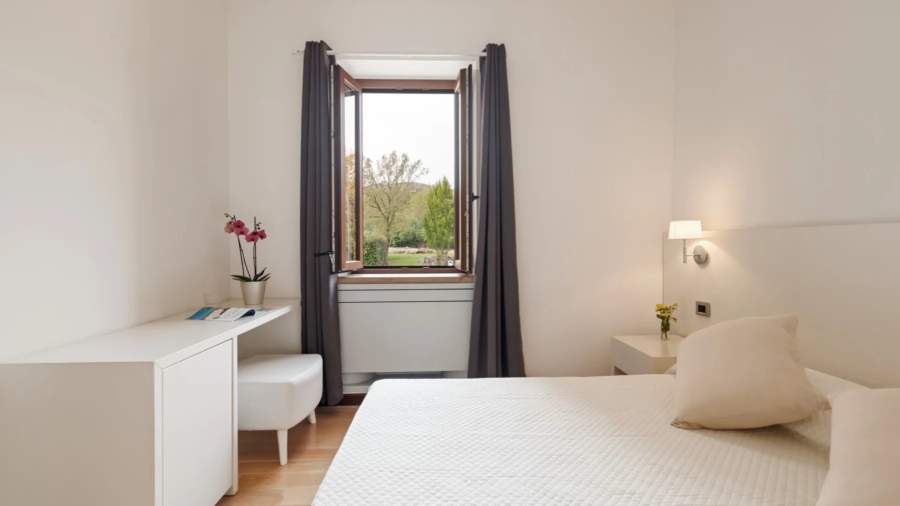 A bright bedroom with a neatly made bed and an open window.