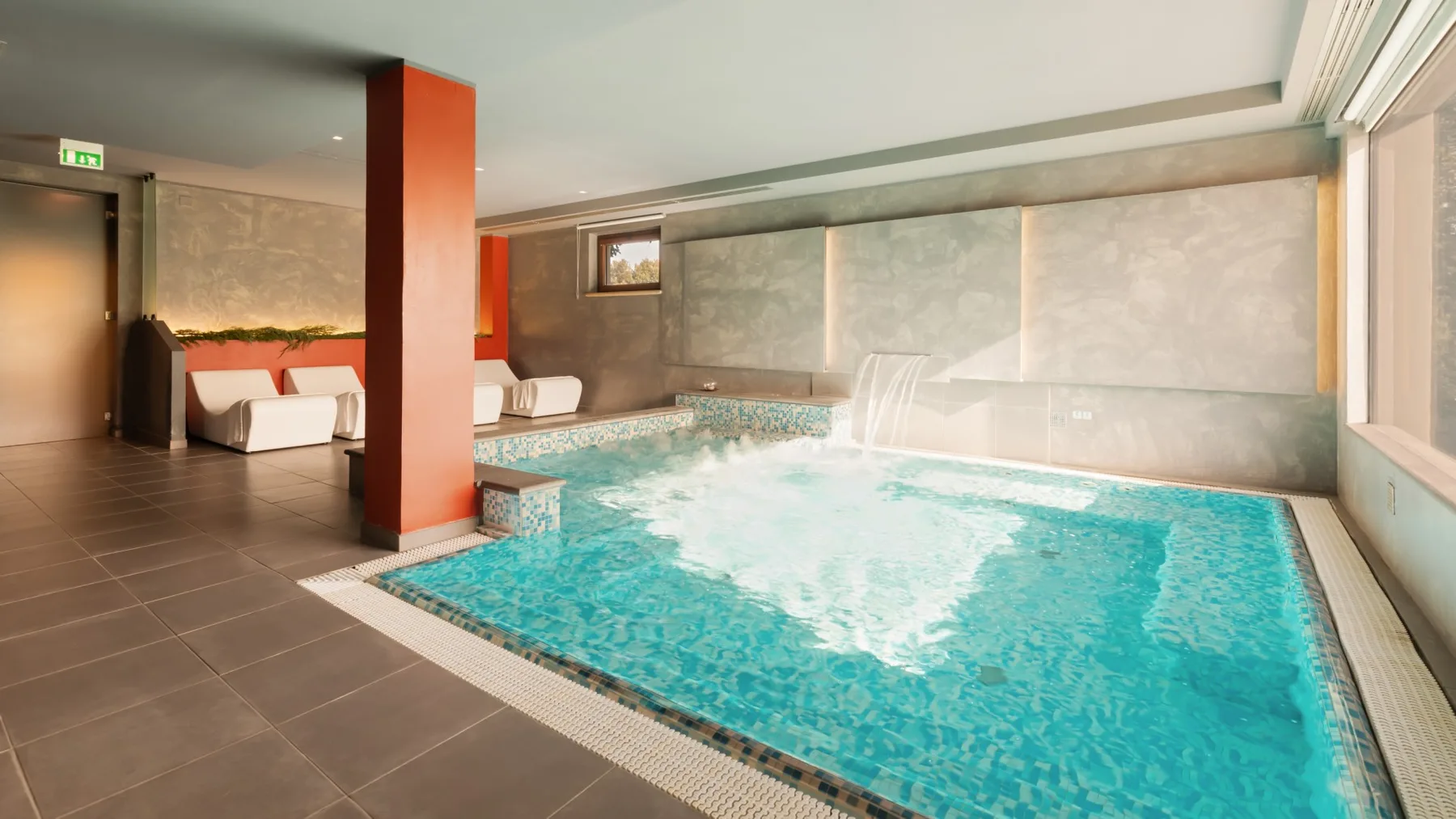 An indoor swimming pool with turquoise water and seating along the wall.