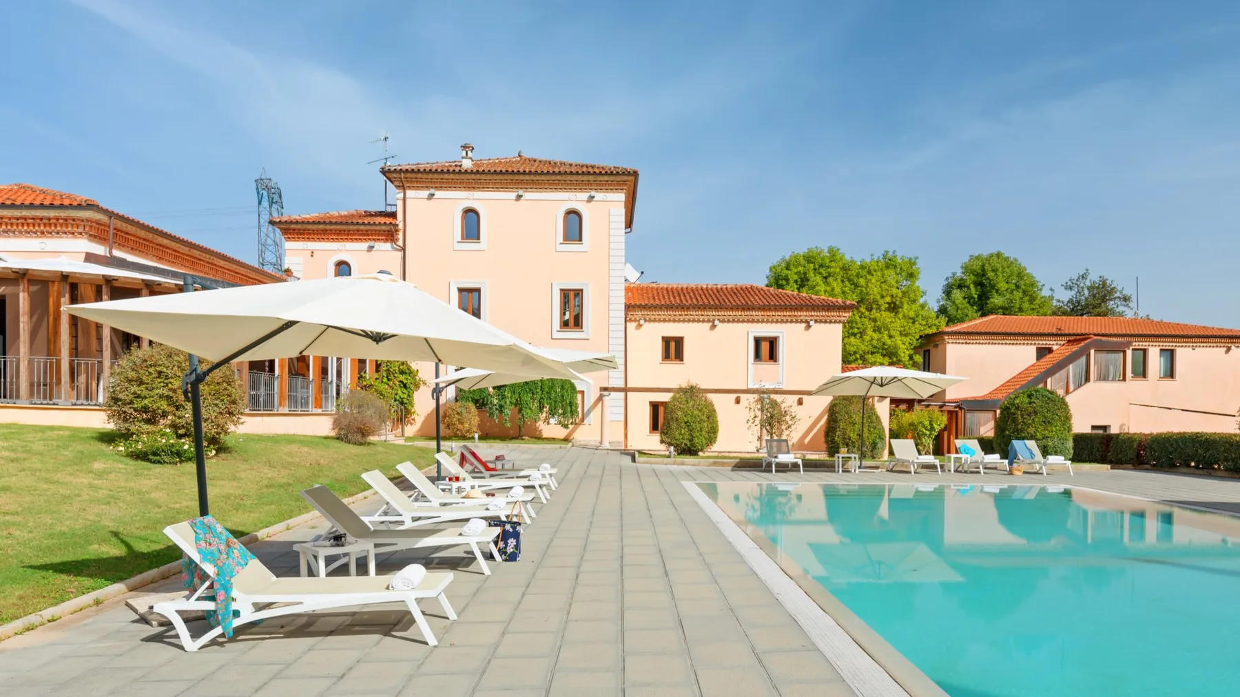 An outdoor swimming pool beside a paved deck with loungers and a pale building.
