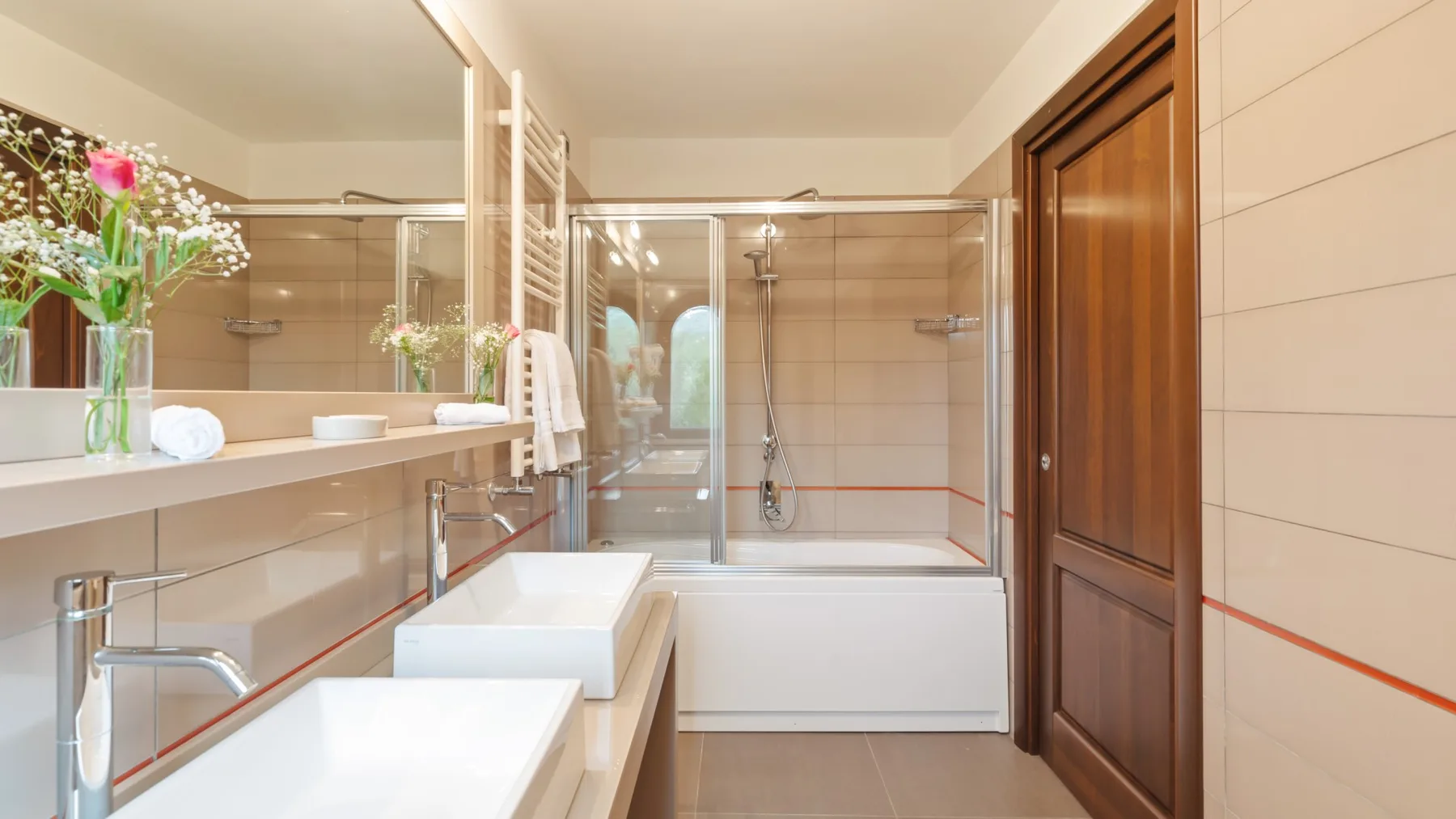 A bright bathroom with a double vanity and a bathtub behind glass.