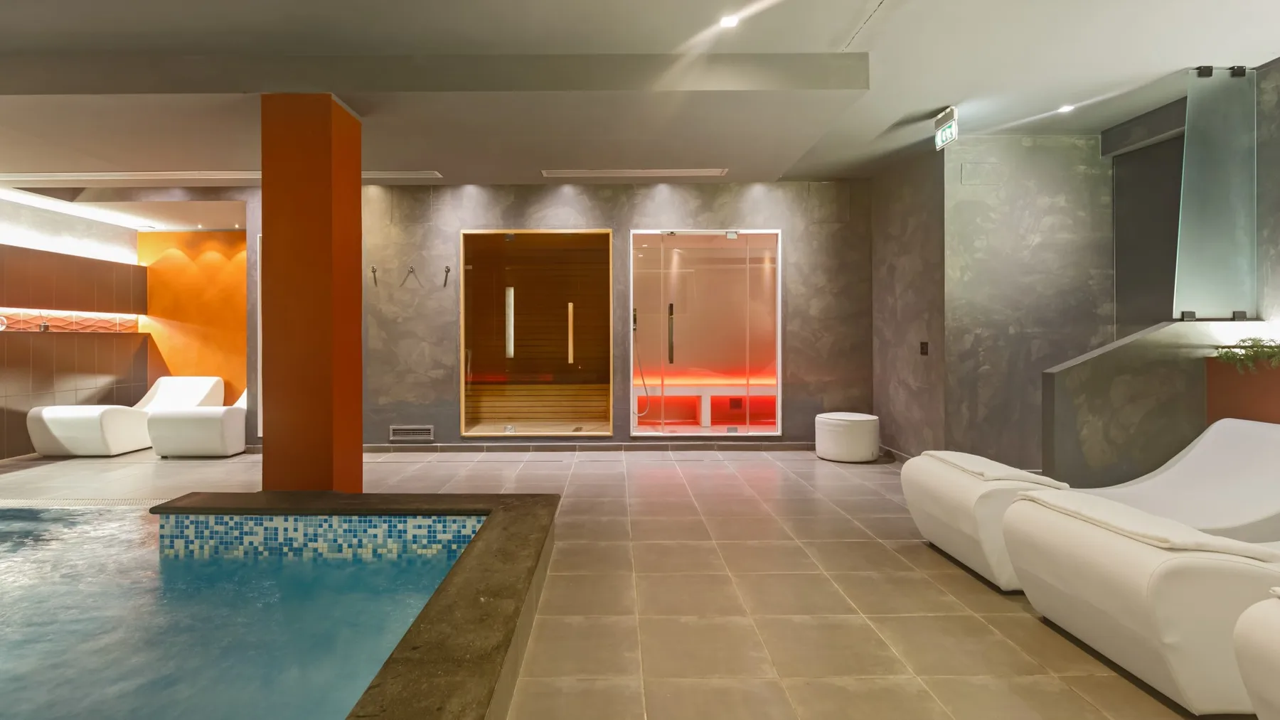 A modern indoor pool area with lounge seating and illuminated wall panels.
