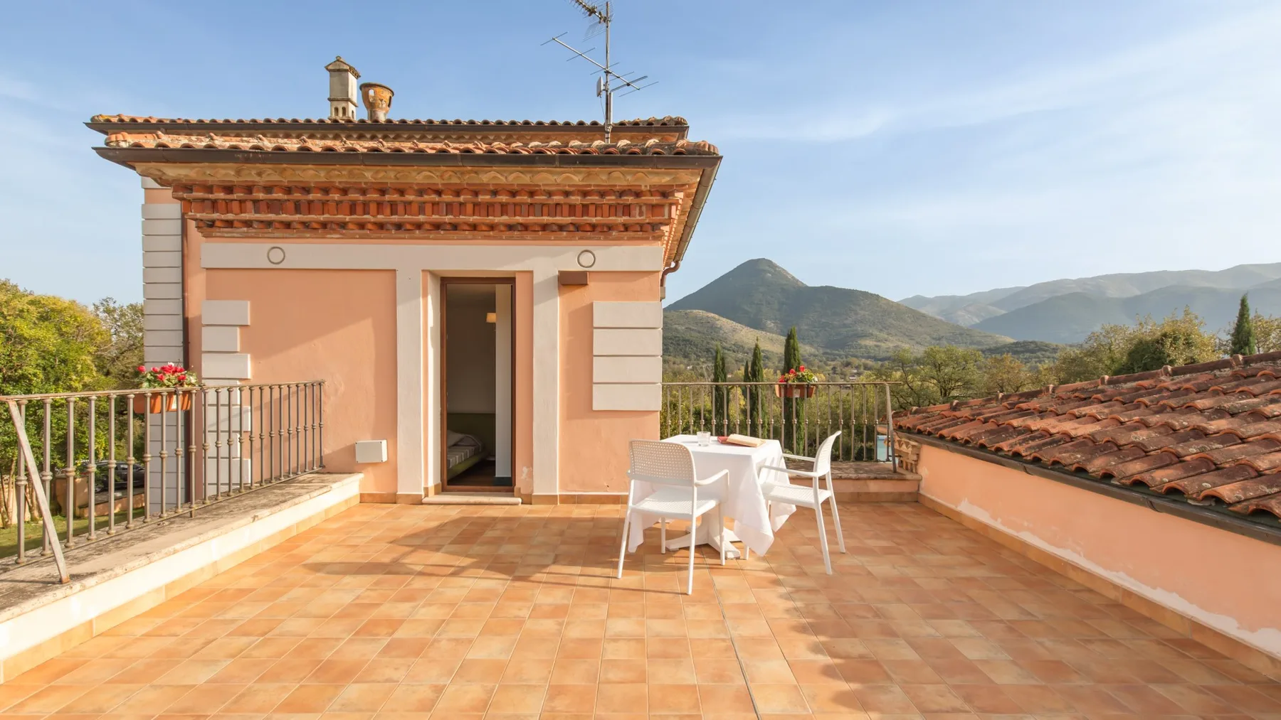 A tiled rooftop terrace with a table and chairs overlooks the surrounding mountains.