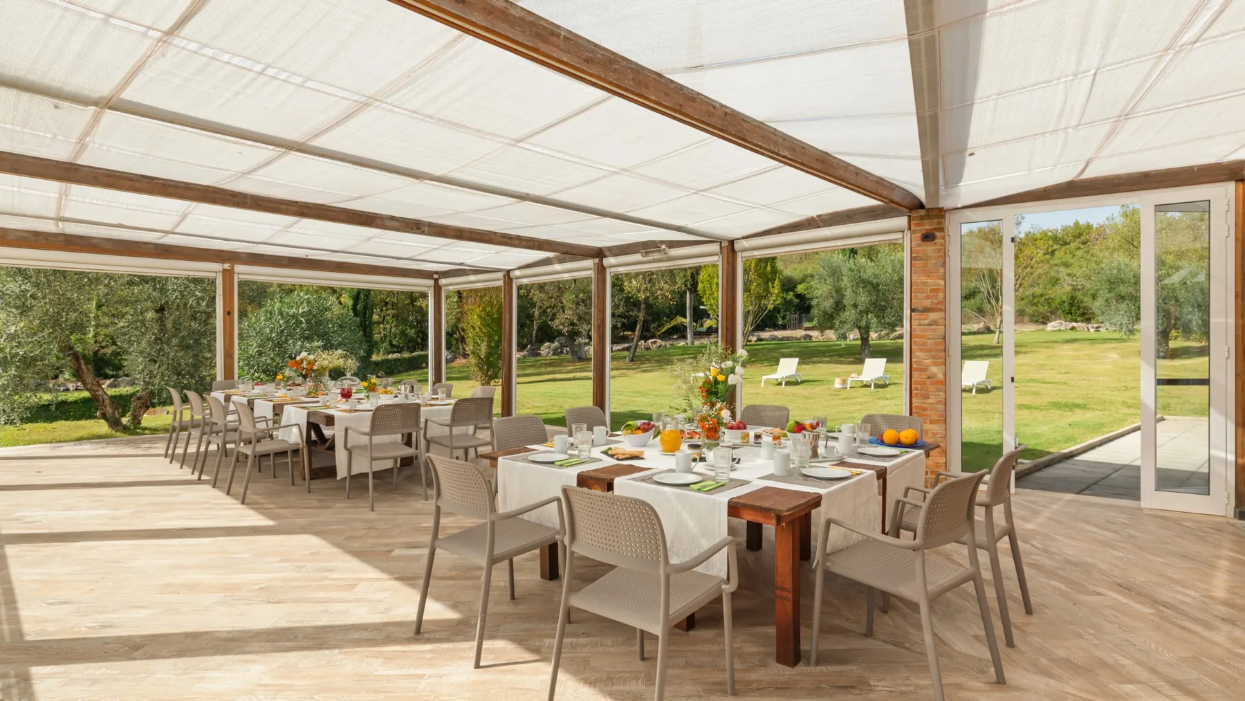 A covered outdoor dining area with tables and seating overlooks a garden.
