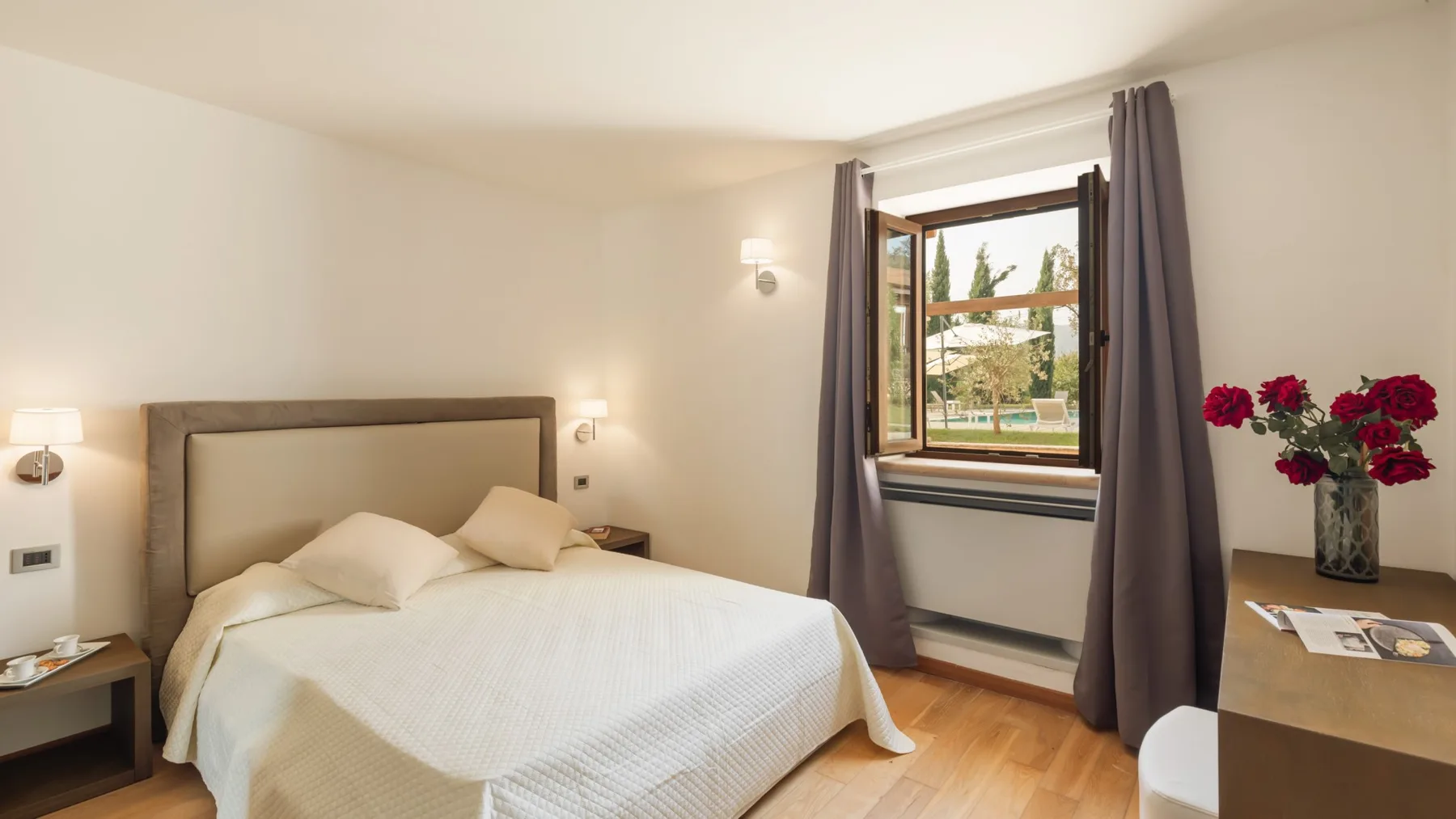A bright bedroom with a neatly made bed and a curtained window.