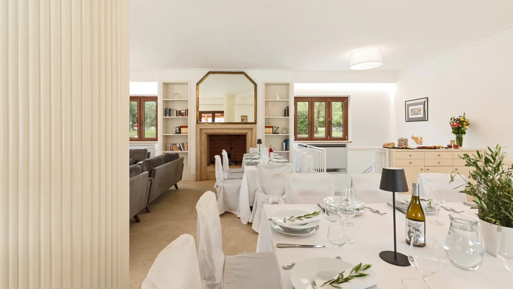 A bright dining room is set with white tablecloths and place settings.