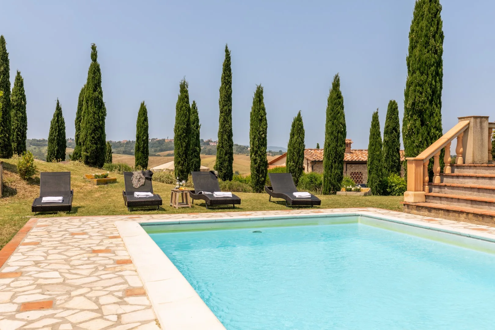 An outdoor swimming pool bordered by a stone-paved patio and lounge seating.