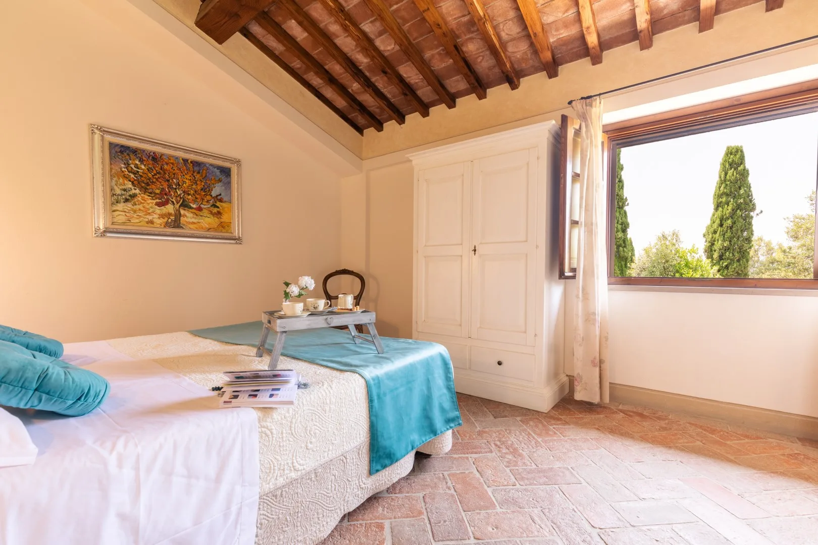 A bedroom with a bed, a small table, and a large window overlooking greenery.