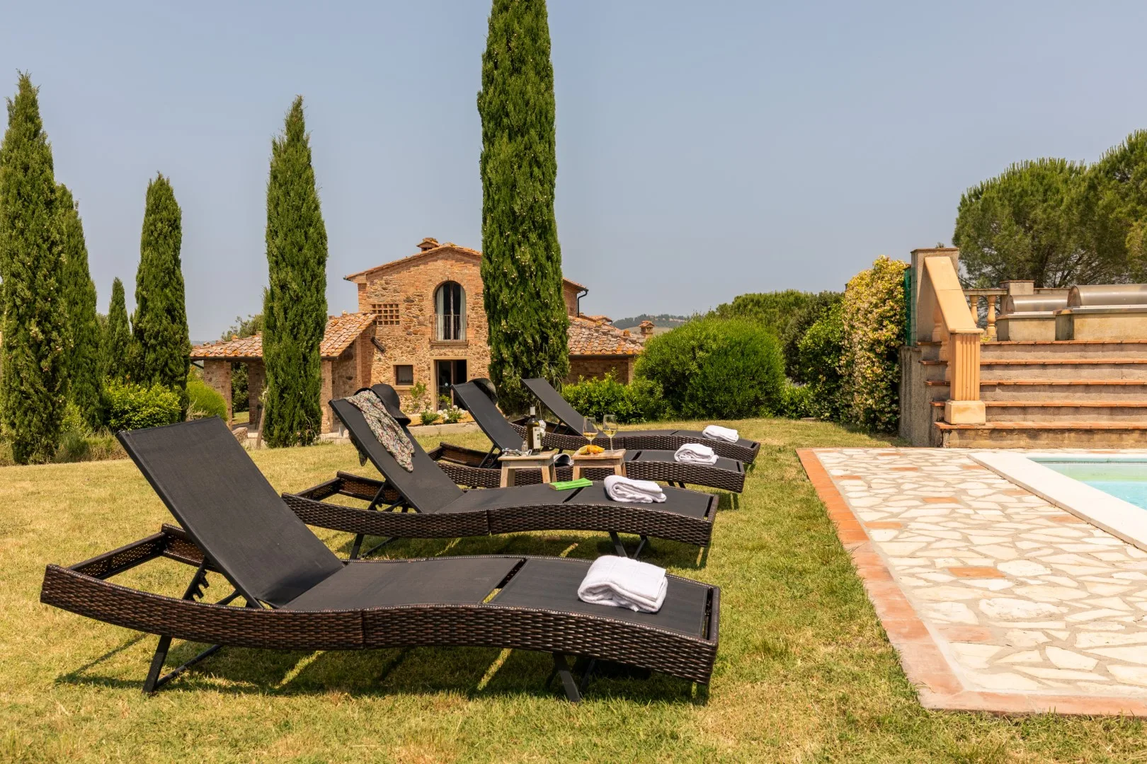 Outdoor lounge area with reclining seating beside a swimming pool and stone path.