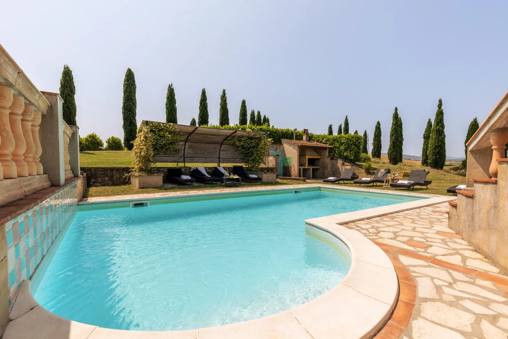 An outdoor swimming pool sits beside a stone-paved patio and garden.