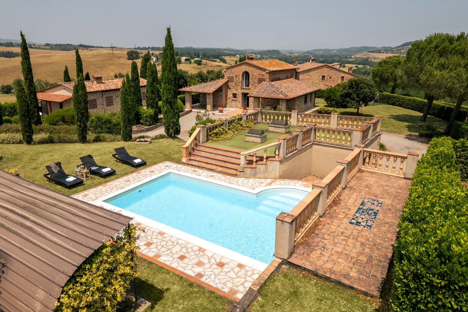 A countryside villa overlooks a swimming pool and landscaped grounds.