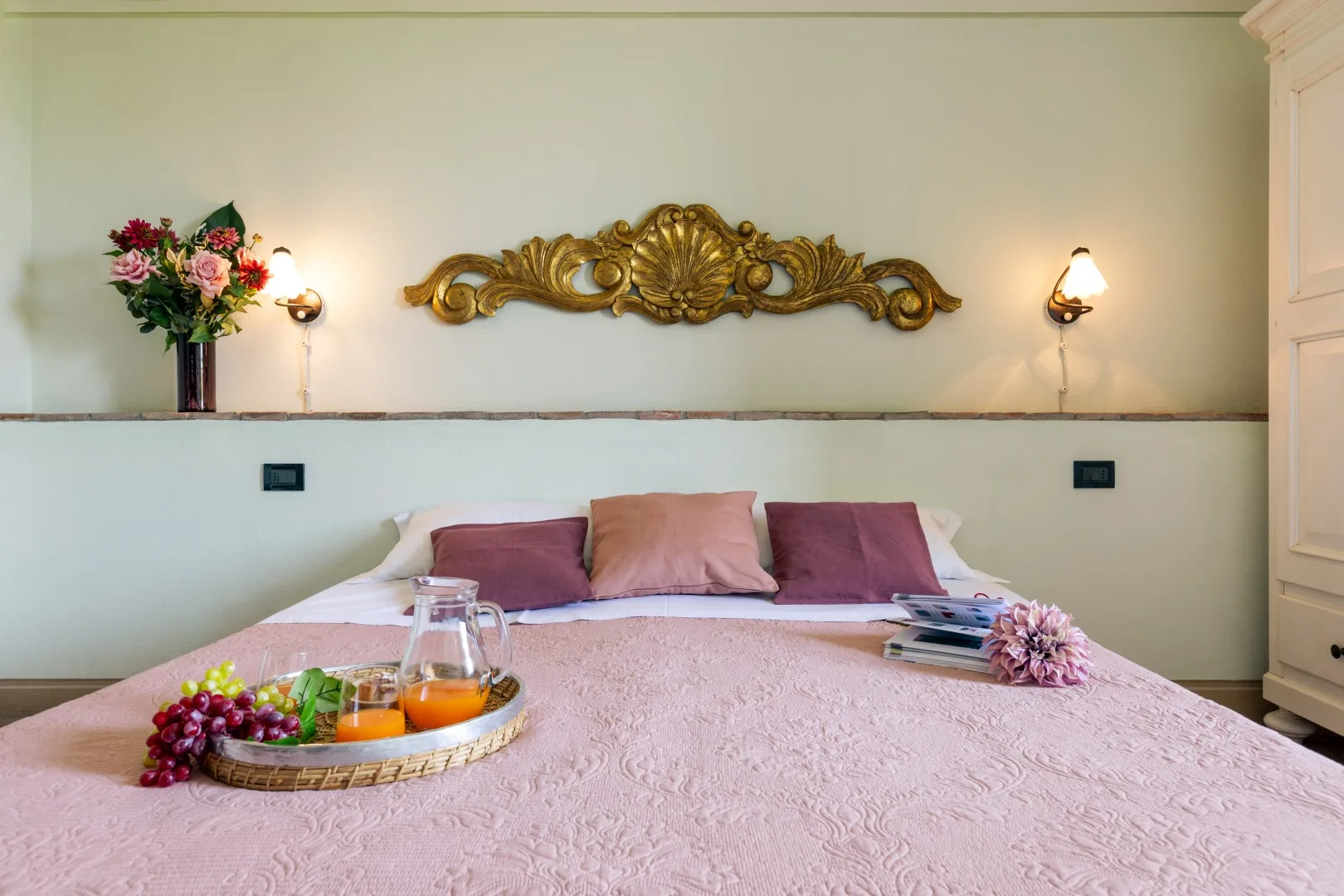 A bedroom with a pink bedspread, decorative pillows, and floral arrangements.