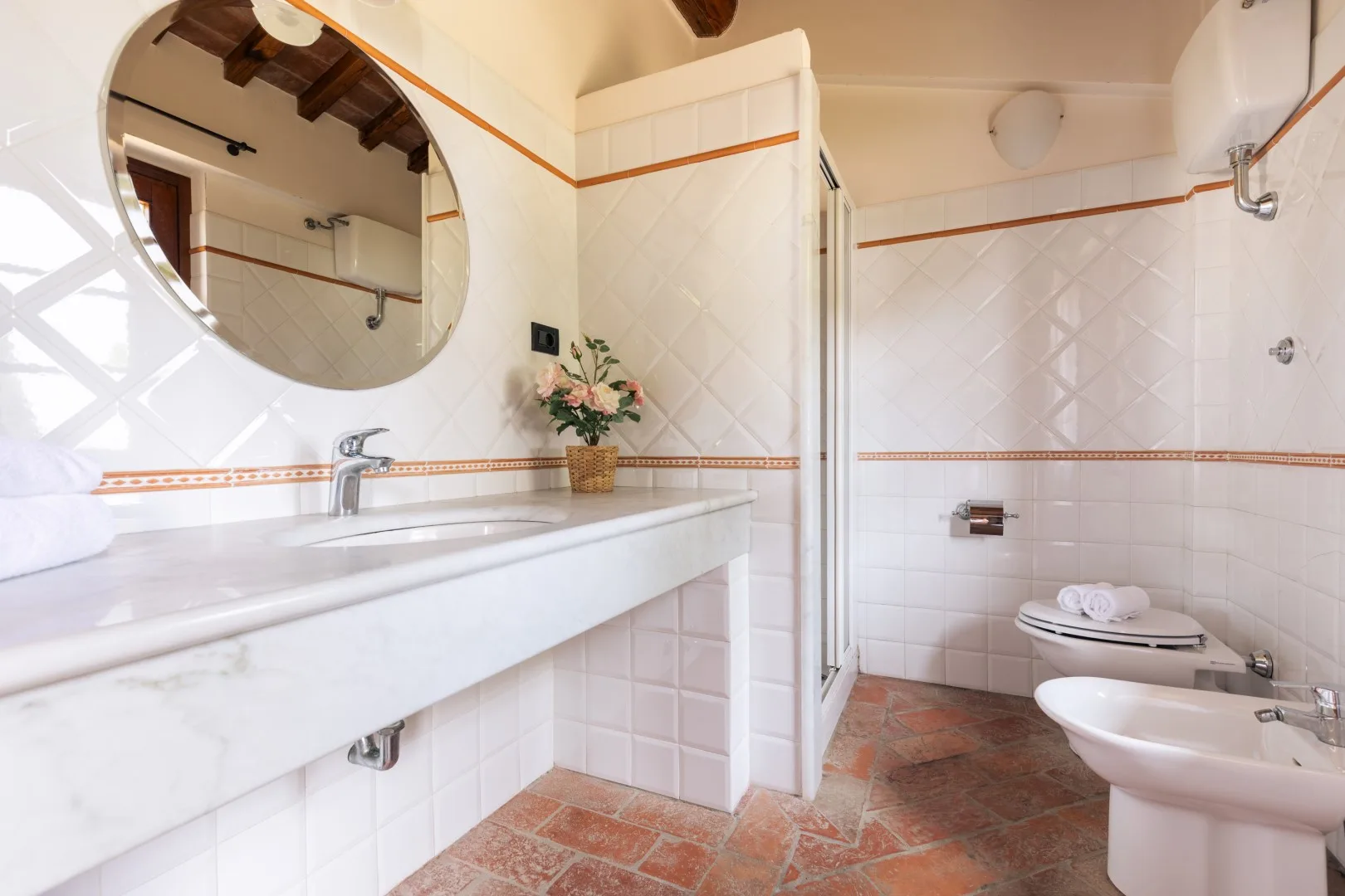 A tiled bathroom with a long sink counter, wall mirror, shower, and toilet.