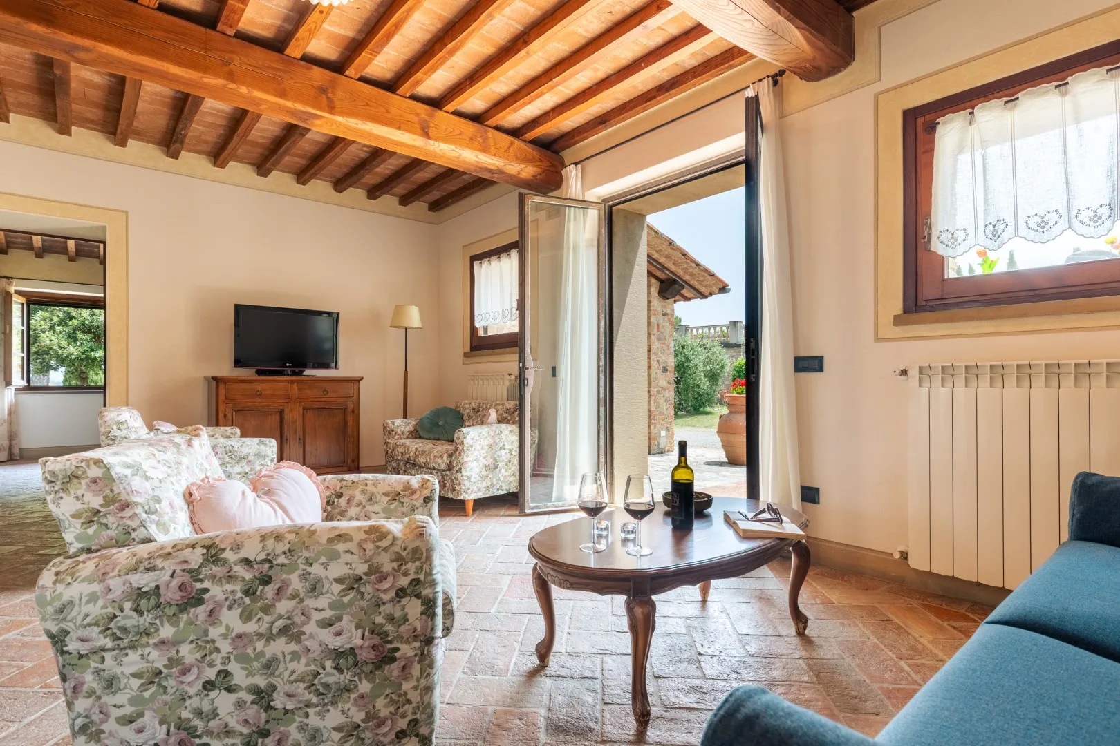 A living room with floral seating, a coffee table, and an open doorway to a patio.