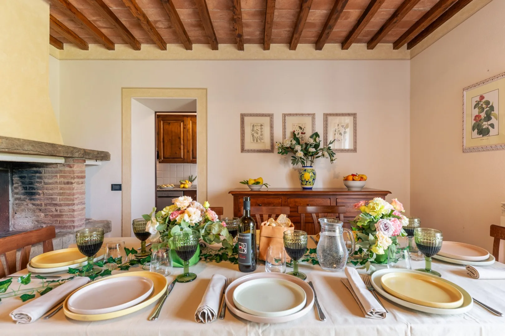 A dining room with a set table and flowers beneath exposed wooden ceiling beams.
