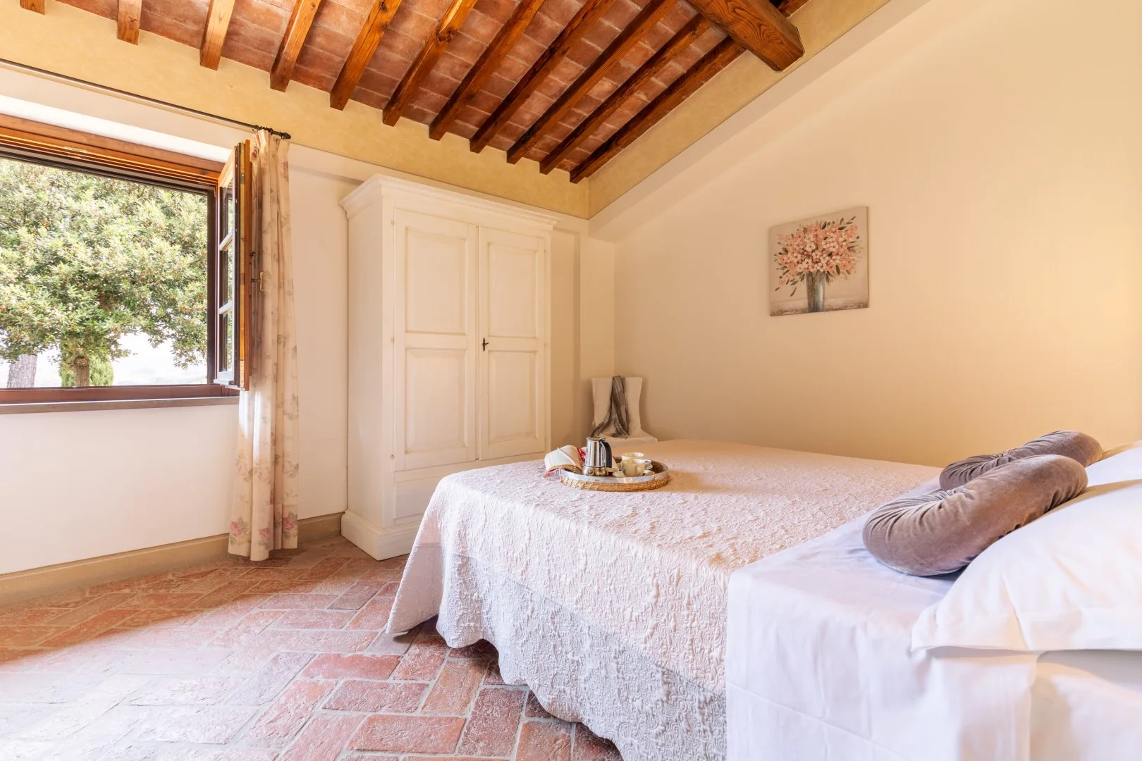A bedroom with a bed, a small table, and an open window beneath exposed wooden beams.