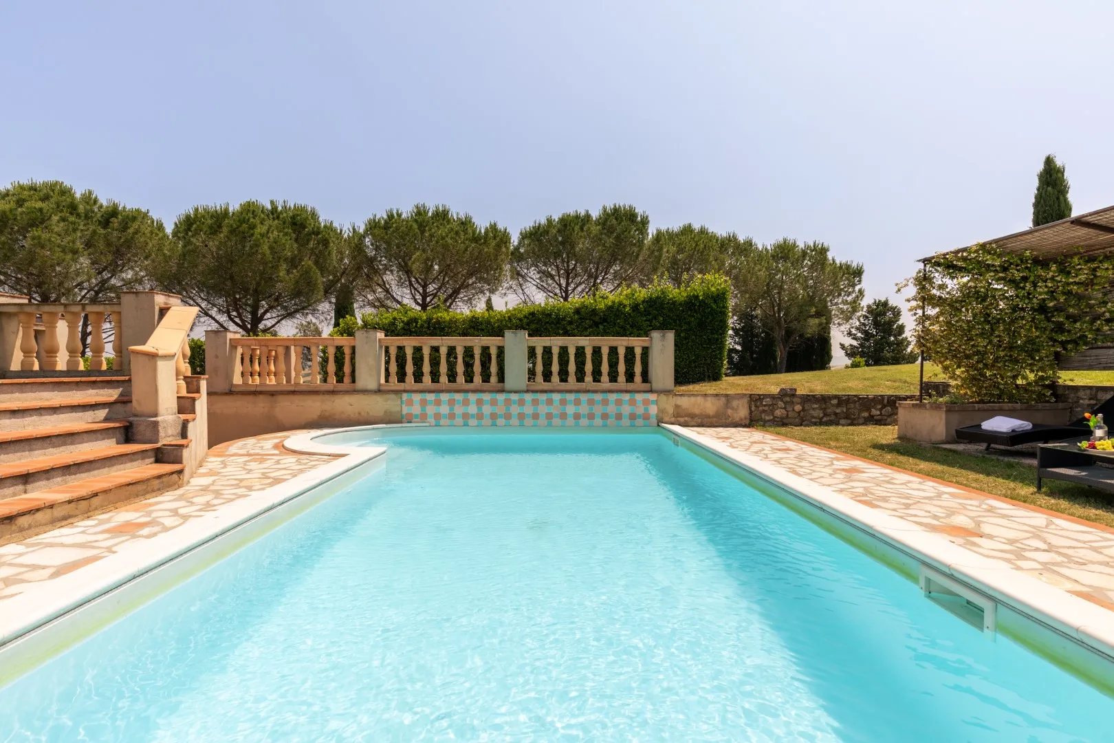 An outdoor swimming pool bordered by a stone terrace, steps, and trees.