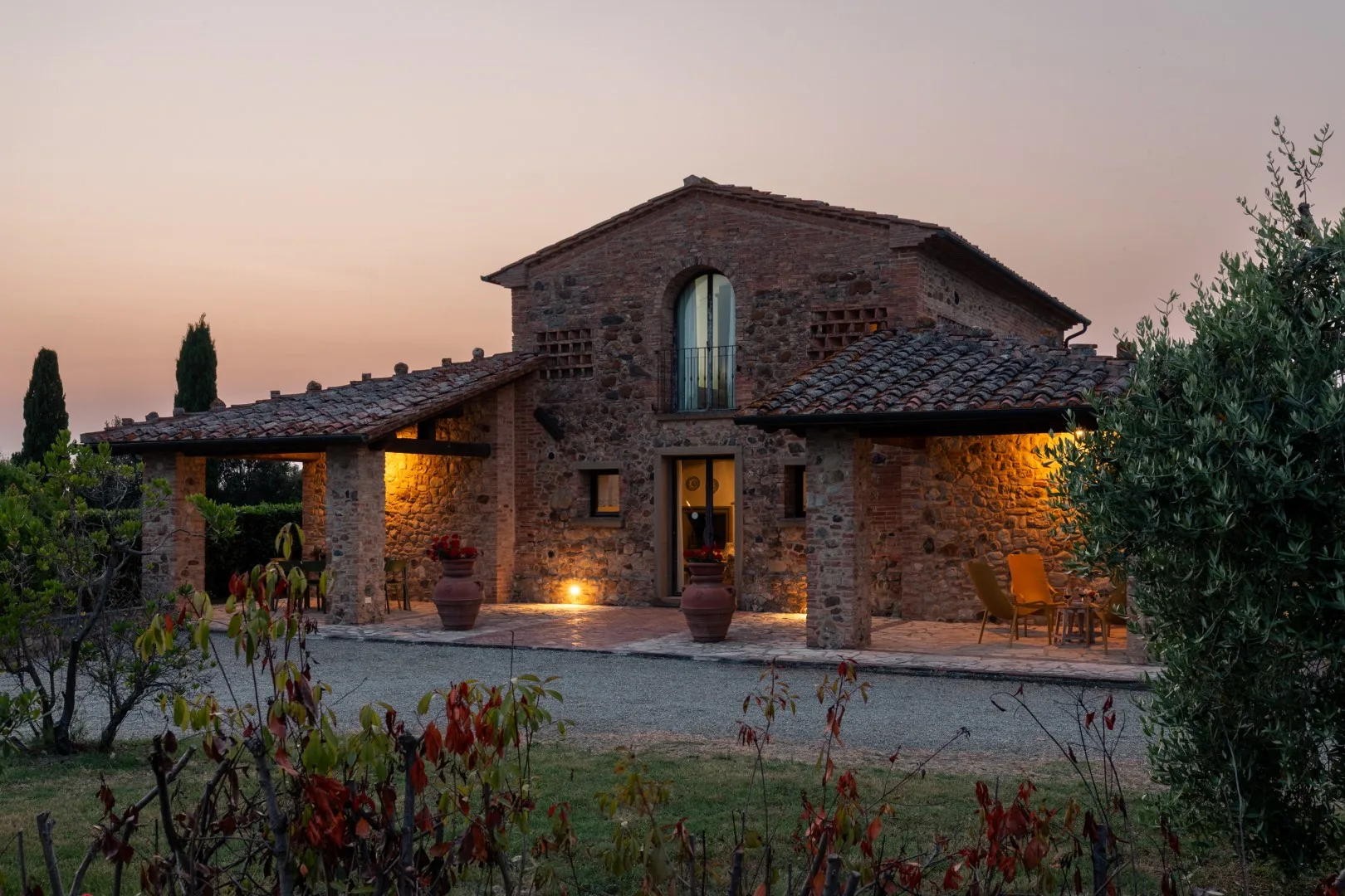 A stone house with a tiled roof and warmly lit entrance at dusk.