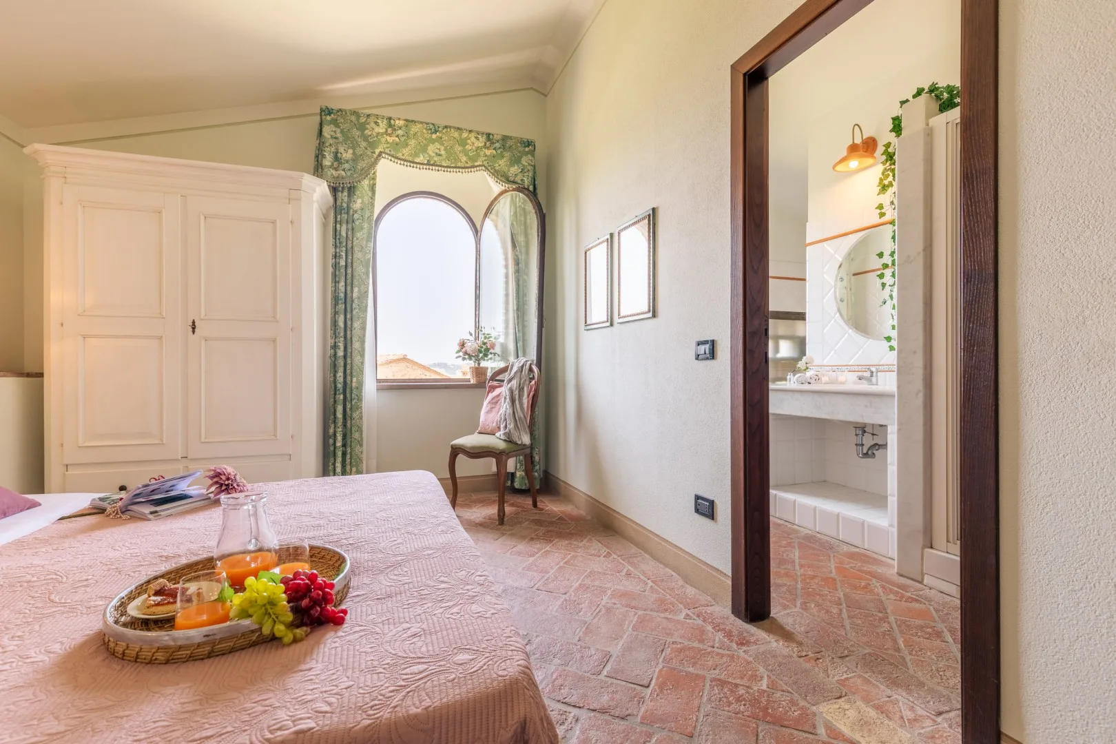 A bedroom with a bed, wardrobe, and an arched window beside a bathroom doorway.