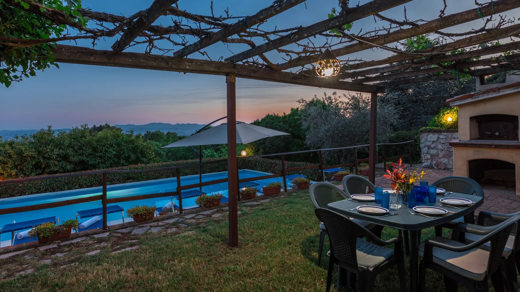 Comedor al aire libre junto a una piscina, bajo una pérgola de madera.