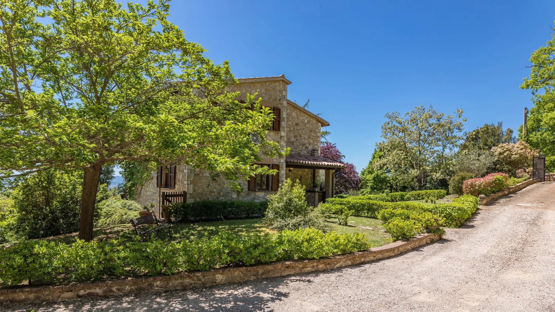 Una casa de piedra está rodeada de jardines junto a un camino pavimentado.