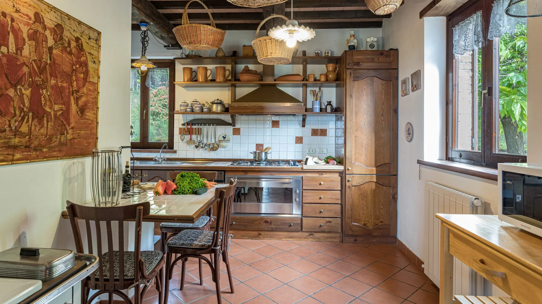 Una cocina rústica con armarios de madera, suelo de baldosas y ventanas con vistas a la vegetación.
