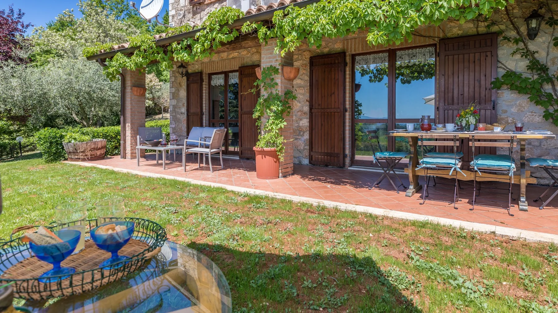 Un patio cubierto de enredaderas con asientos al aire libre y una mesa junto al jardín.