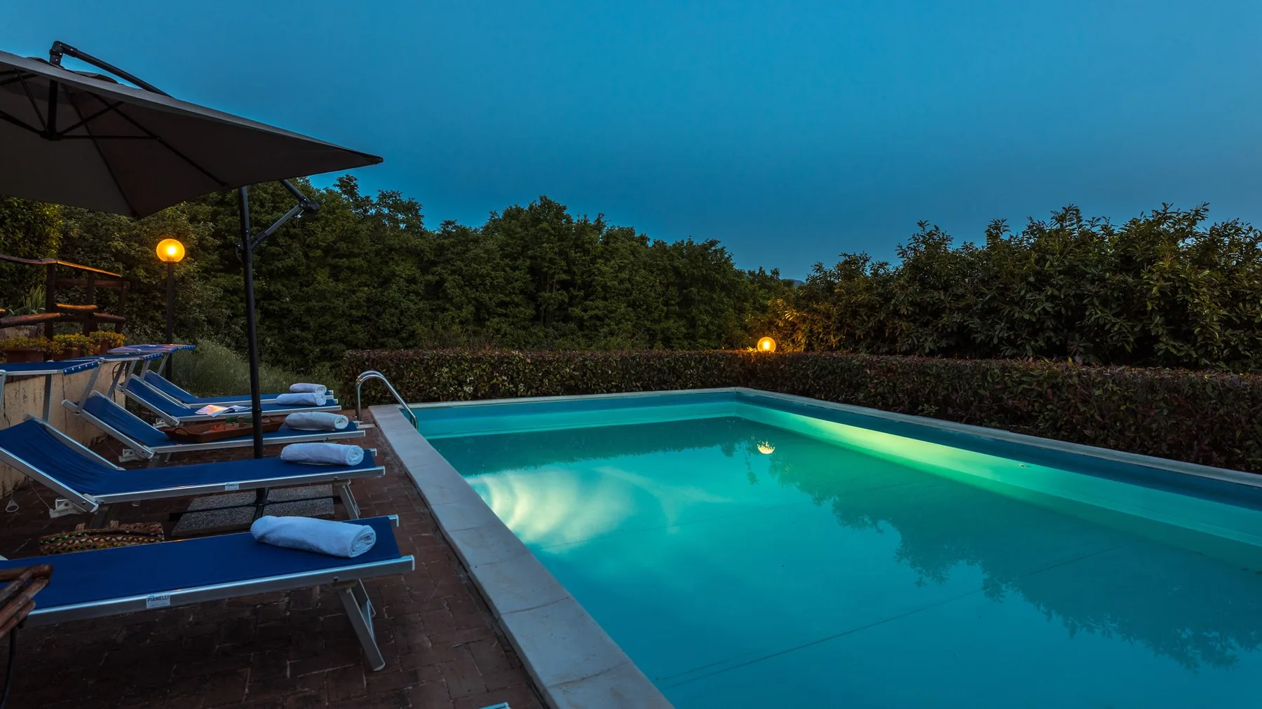 Una piscina exterior iluminada al atardecer junto a asientos reclinables.
