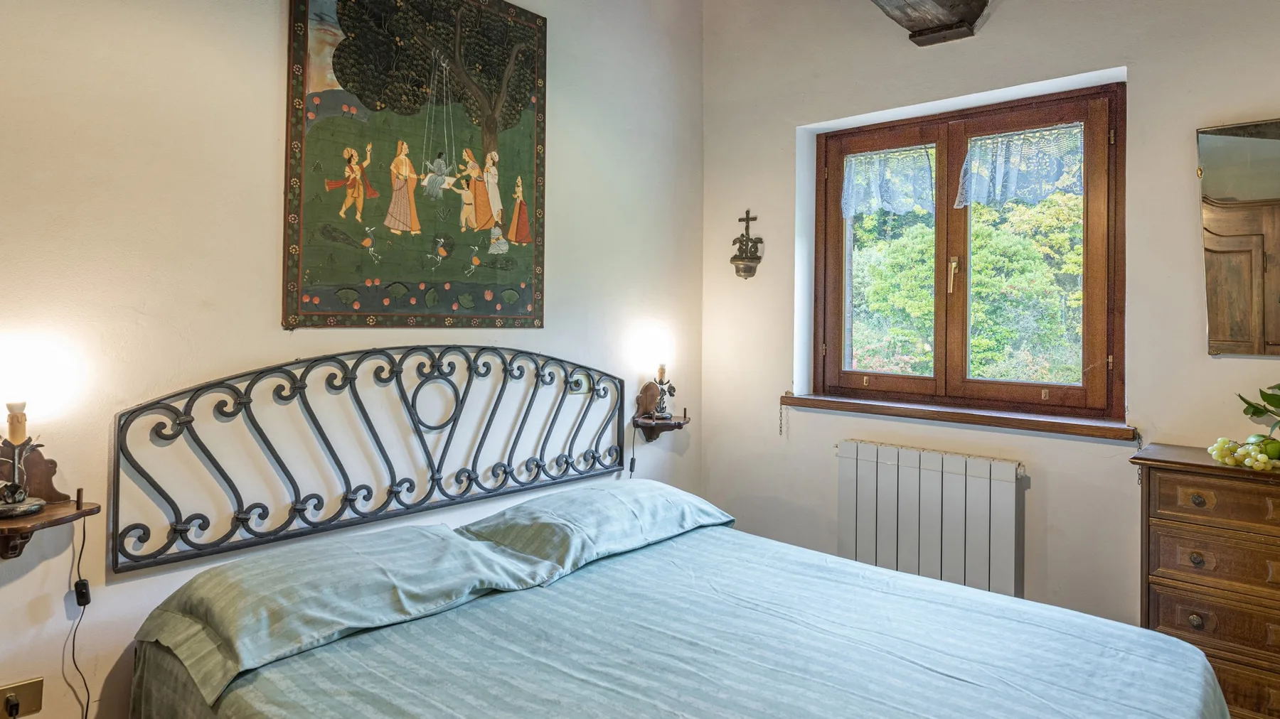 Un dormitorio con una cama bajo un tapiz decorativo y una ventana con vistas a la vegetación.