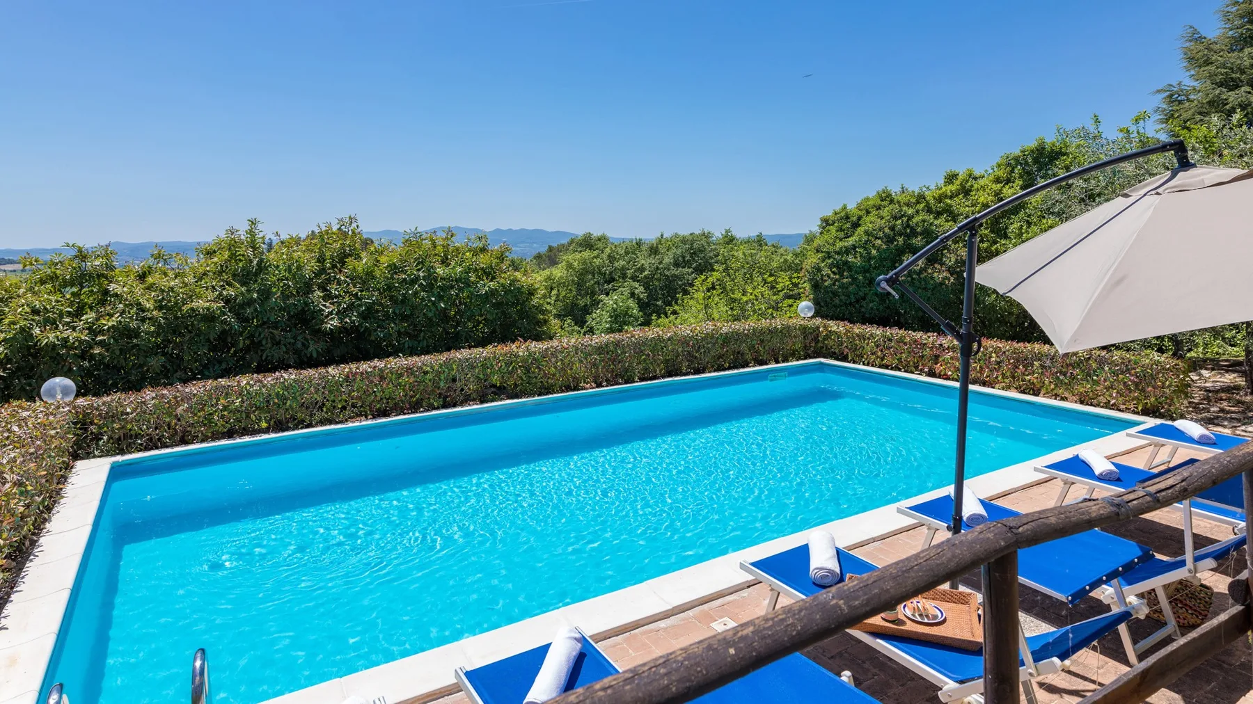 Una piscina luminosa está rodeada de tumbonas azules y vegetación.
