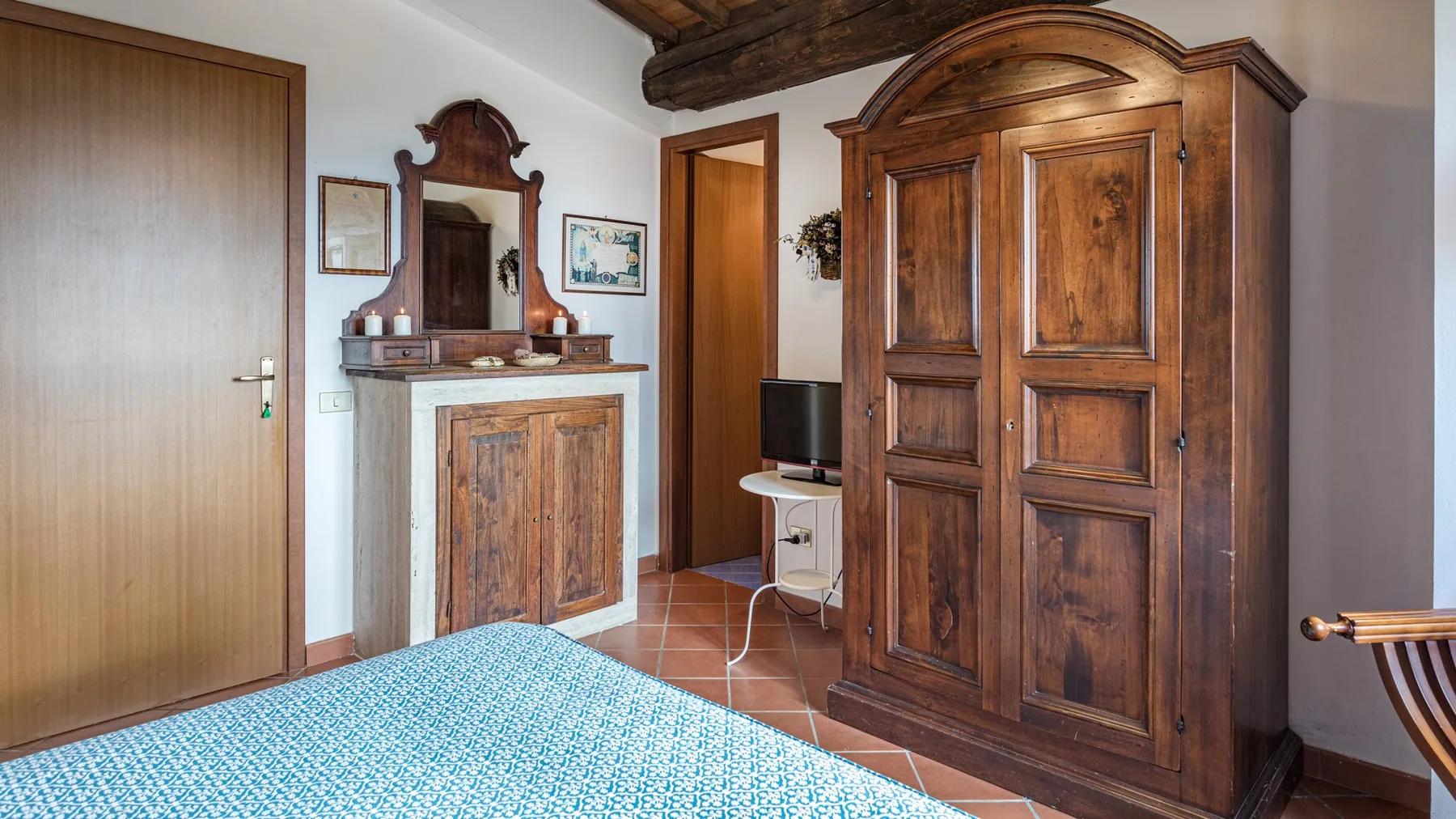Un dormitorio con una cama de madera, suelo de baldosas y un gran armario tallado.