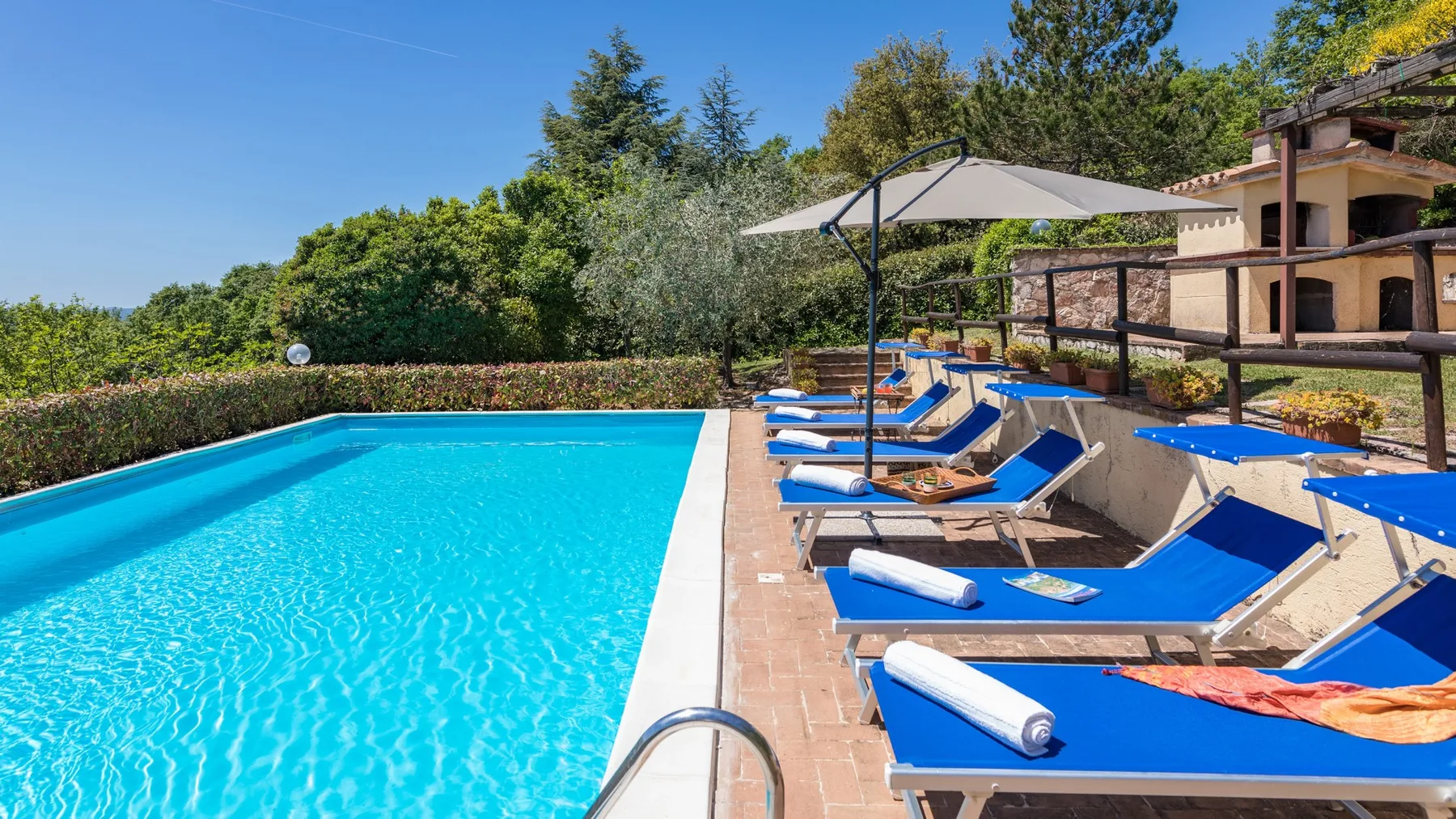 Una piscina al aire libre está junto a tumbonas azules y una gran sombrilla.