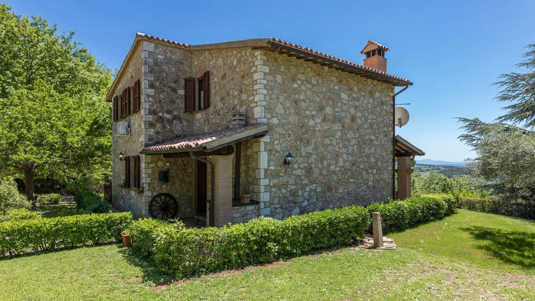 Una casa de piedra se alza tras un seto bajo en un césped soleado.
