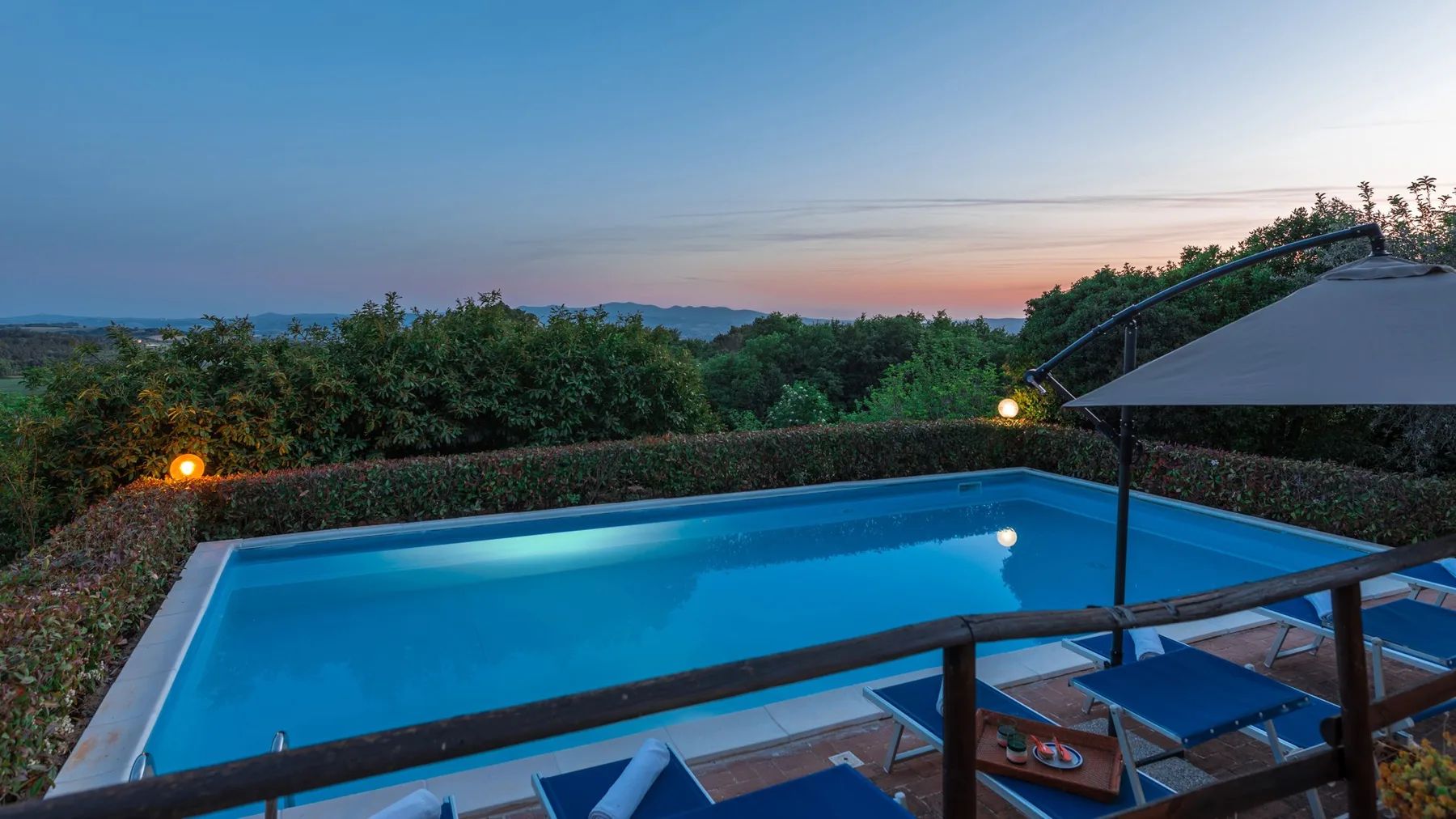Una piscina al aire libre da a árboles verdes bajo un cielo colorido al atardecer.