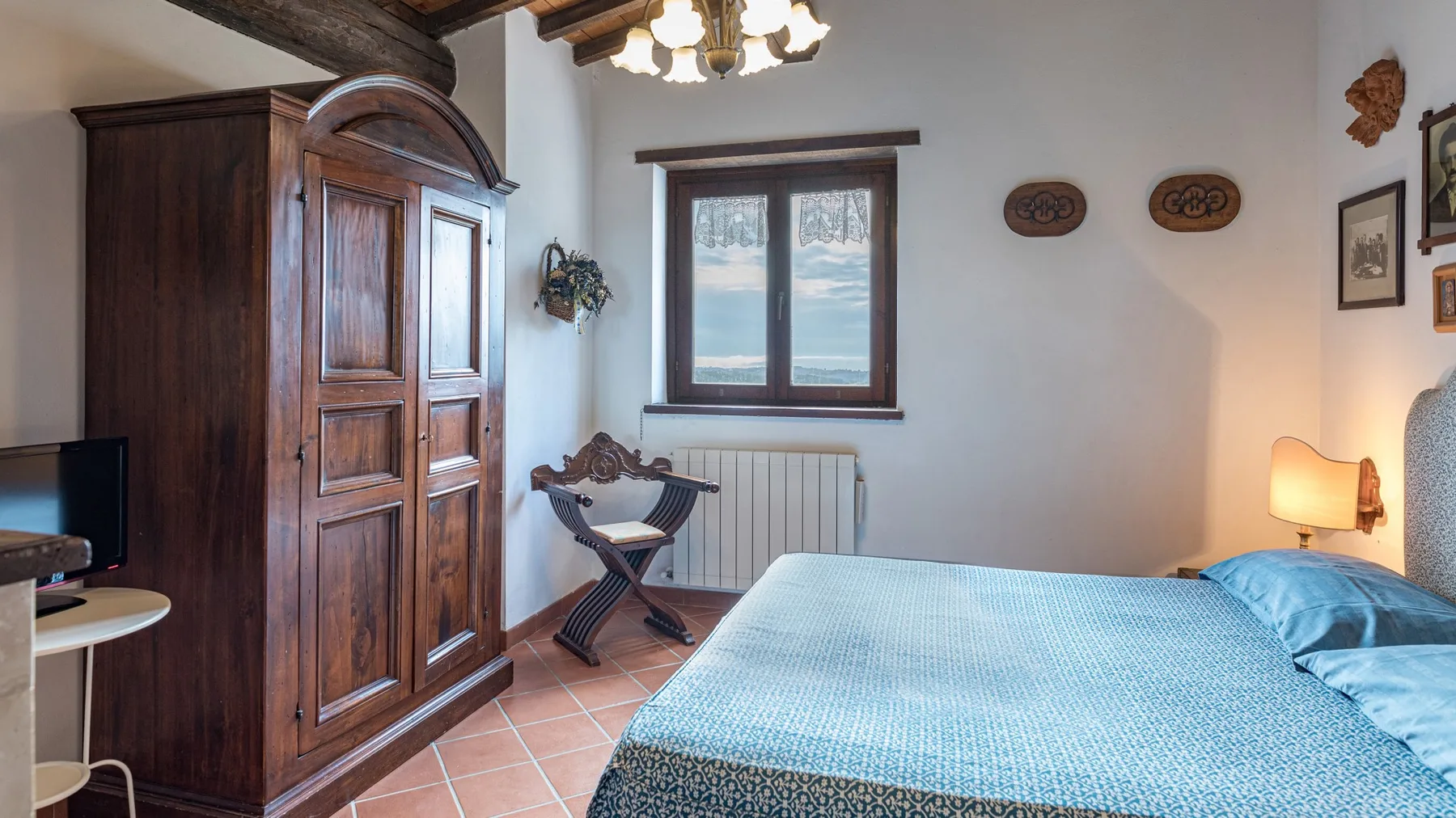 Un dormitorio con una colcha azul, un armario de madera y una ventana.
