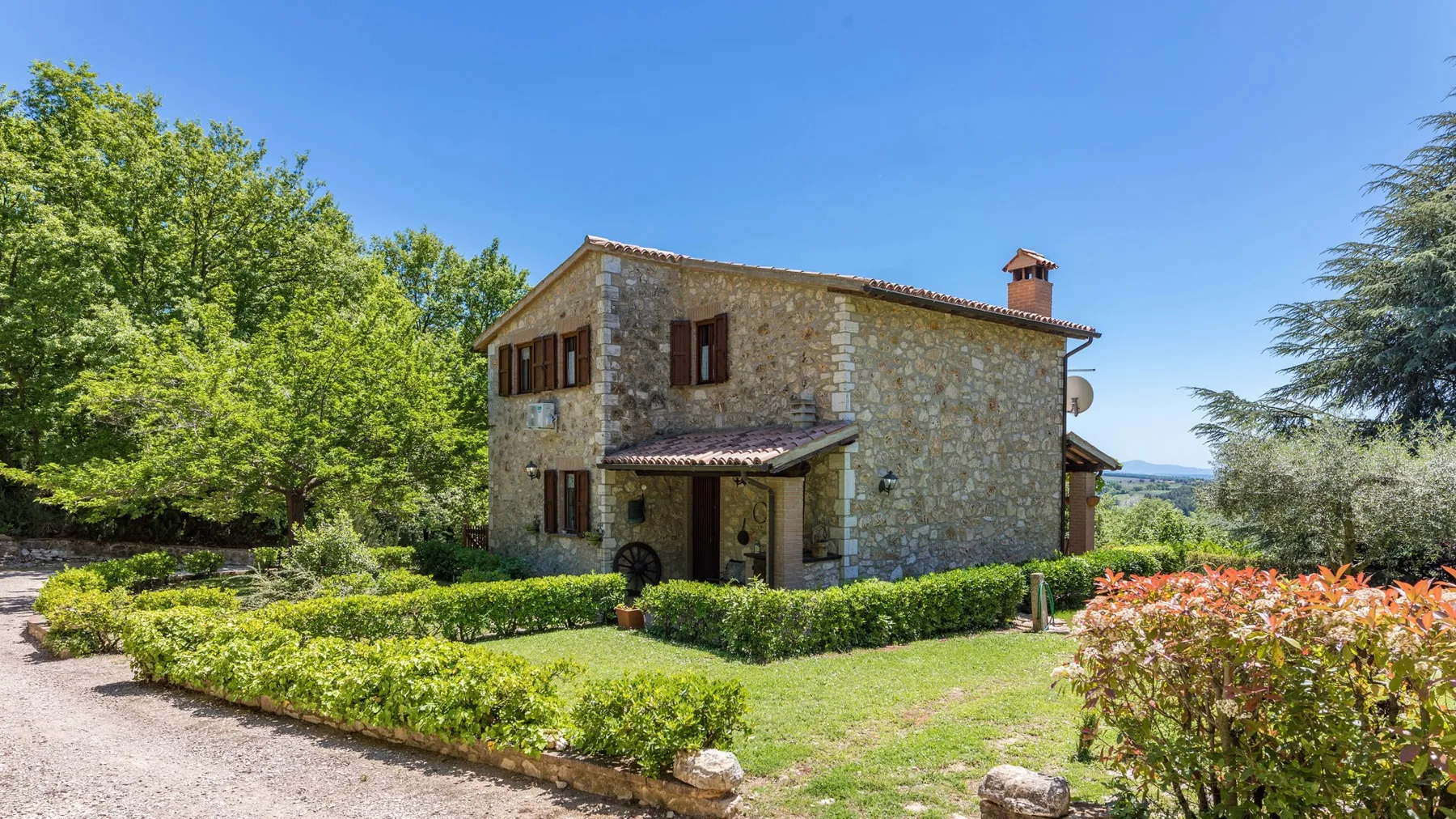 Una casa de piedra está junto a un jardín con setos y un camino de grava.