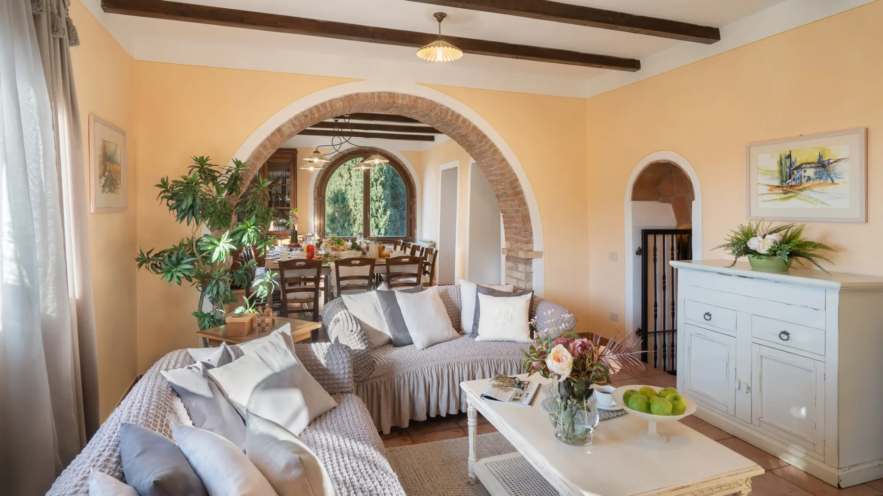 Una sala luminosa con asientos, una mesa de centro y un comedor al otro lado de un arco.