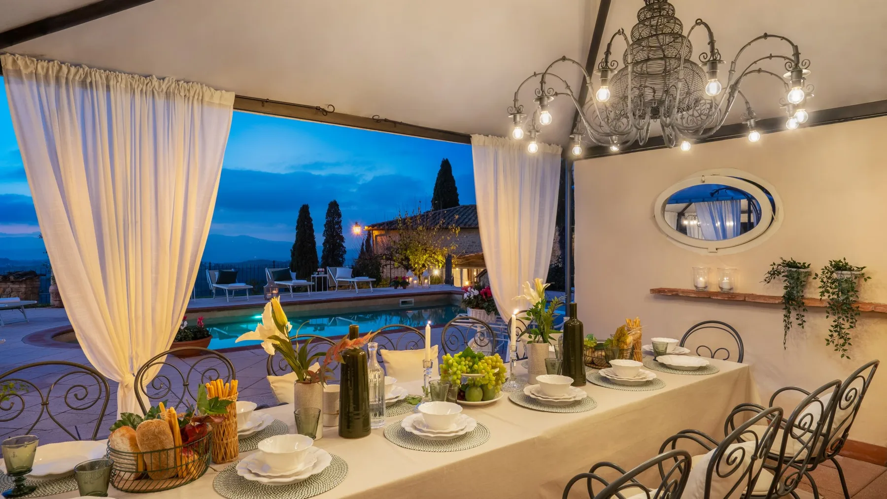 Una mesa está preparada junto a cortinas abiertas, con vistas a una piscina y un jardín.